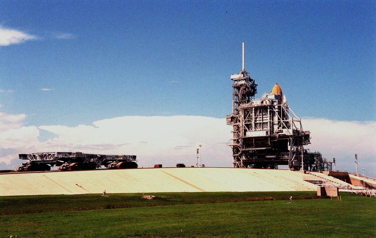 (Left) The crawler transporter makes its way across Launch Pad 39-B to the Mobile Launch Platform and Space Shuttle Discovery to await possible orders for a rollback. KSC managers developed a precautionary plan to roll back Discovery to the Vehicle Assembly Building in the event that Hurricane Georges threatens Central Florida. The decision was made to minimize risk and provide protection to the Space Shuttle national asset