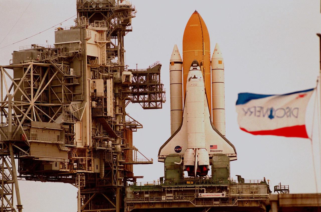 In this close-up, Space Shuttle Discovery sits atop the Mobile Launch Platform on Launch Pad 39-B, with the Rotating Service Structure moved back, to await rollback decision. The flag at right shows the increased wind blowing out of the south. KSC managers developed a precautionary plan to roll back Discovery to the Vehicle Assembly Building in the event that Hurricane Georges threatens Central Florida. The decision was made in order to minimize risk and provide protection to the Space Shuttle, a national asset