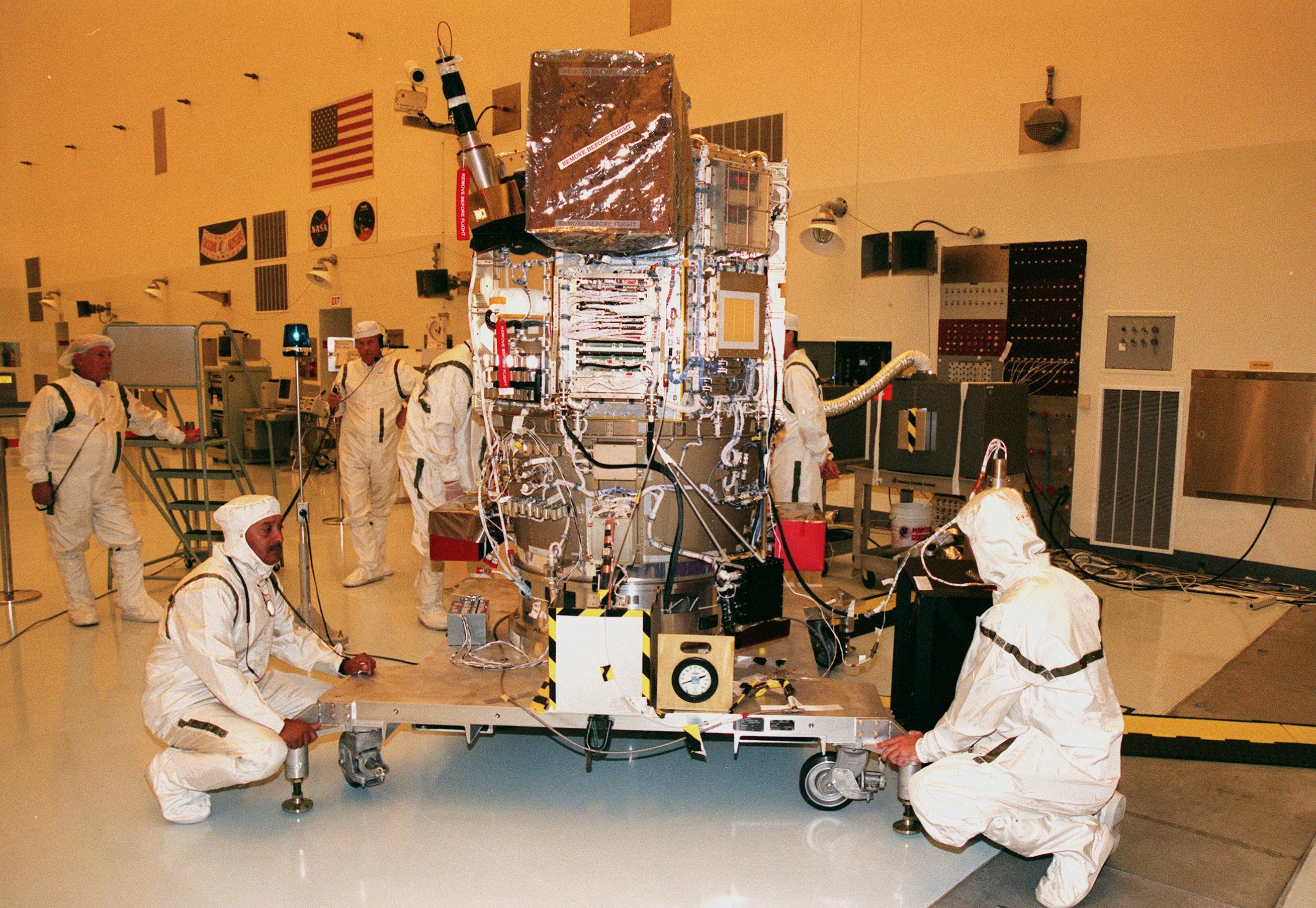Six people in white protective suits surround a NASA spacecraft that is secured atop a wheeled work stand at NASA's Kennedy Space Center in Florida. Photo credit: NASA