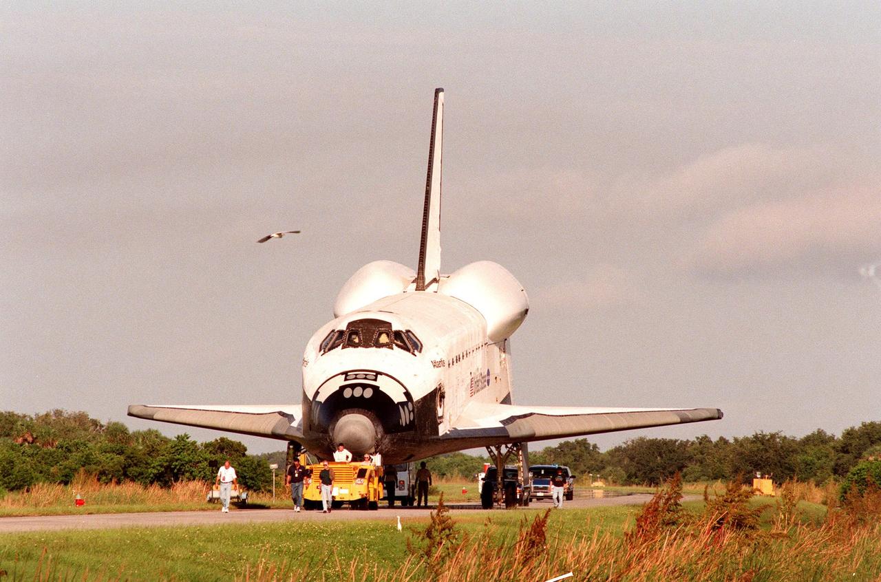 The orbiter Atlantis is towed away from the Shuttle Landing Facility after returning home from California atop its Shuttle Carrier Aircraft. The orbiter spent 10 months in Palmdale undergoing extensive inspections and modifications in the orbiter processing facility there. The modifications included several upgrades enabling it to support International Space Station missions, such as adding an external airlock for ISS docking missions and installing thinner, lighter thermal protection blankets for weight reduction which will allow it to haul heavier cargo. Atlantis will undergo preparations in the Orbiter Processing Facility at KSC for its planned flight in June 1999
