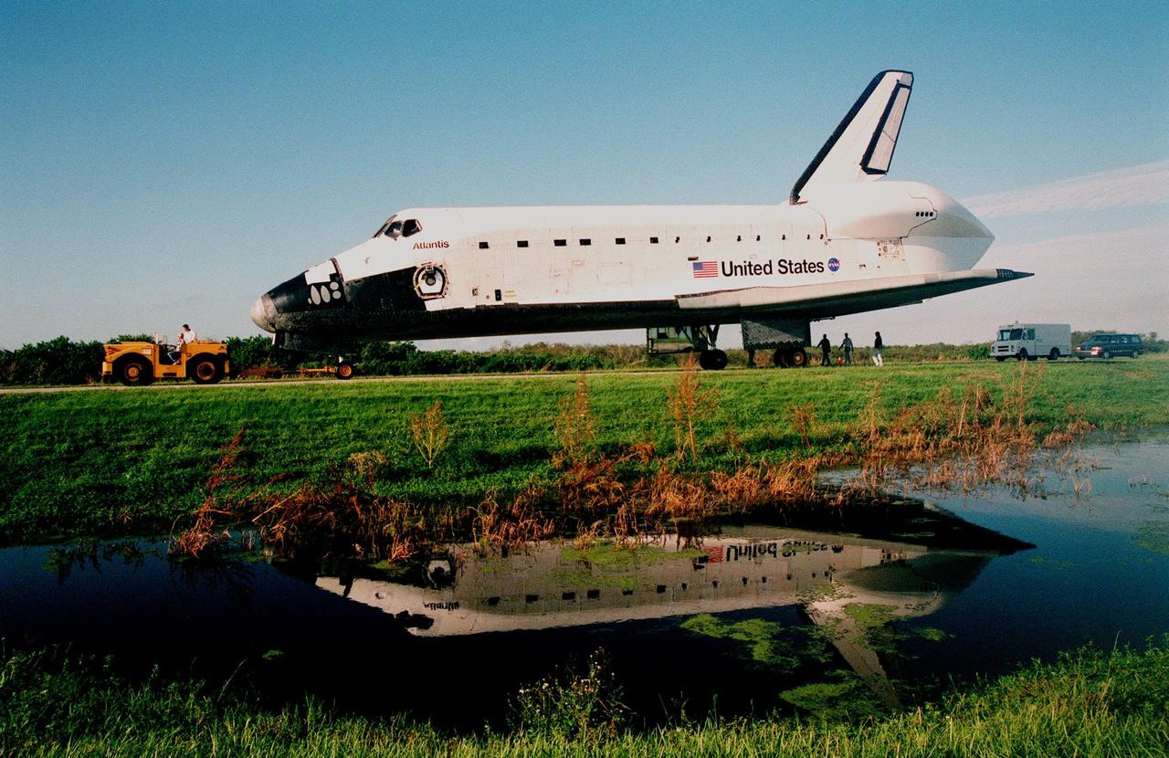 The orbiter Atlantis, being towed from the Shuttle Landing Facility, is reflected in waters from the Banana Creek next to the towway. The orbiter spent 10 months in Palmdale, CA, undergoing extensive inspections and modifications in the orbiter processing facility there. The modifications included several upgrades enabling it to support International Space Station missions, such as adding an external airlock for ISS docking missions and installing thinner, lighter thermal protection blankets for weight reduction which will allow it to haul heavier cargo. Atlantis will undergo preparations in the Orbiter Processing Facility at KSC for its planned flight in June 1999
