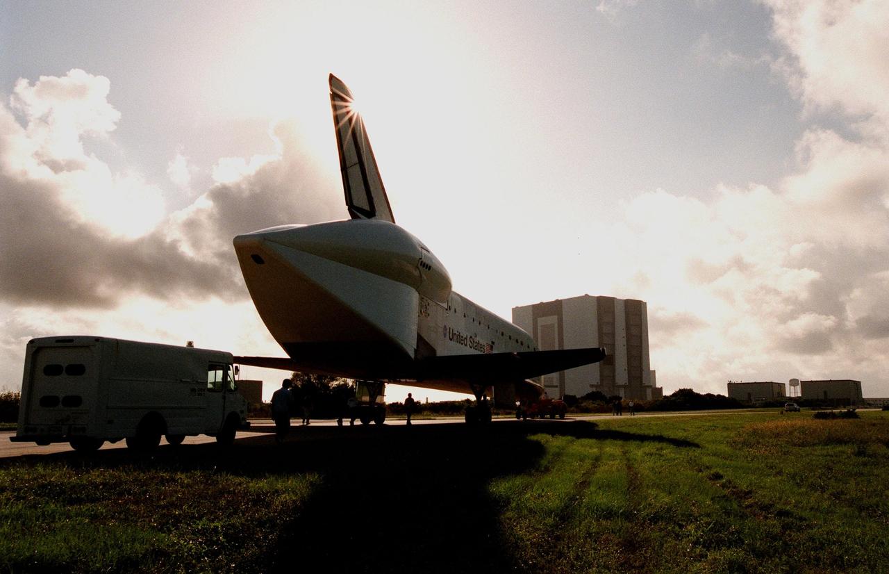 The orbiter Atlantis, being towed from the Shuttle Landing Facility toward the Vehicle Assembly Building (VAB) , intersects the morning sun's rays. In the background, to the right of the VAB, are the Orbiter Processing Facility 1 and 2. Atlantis spent 10 months in Palmdale, CA, undergoing extensive inspections and modifications in the orbiter processing facility there. The modifications included several upgrades enabling it to support International Space Station missions, such as adding an external airlock for ISS docking missions and installing thinner, lighter thermal protection blankets for weight reduction which will allow it to haul heavier cargo. Atlantis will undergo preparations at KSC in Orbiter Processing Facility 2 for its planned flight in June 1999