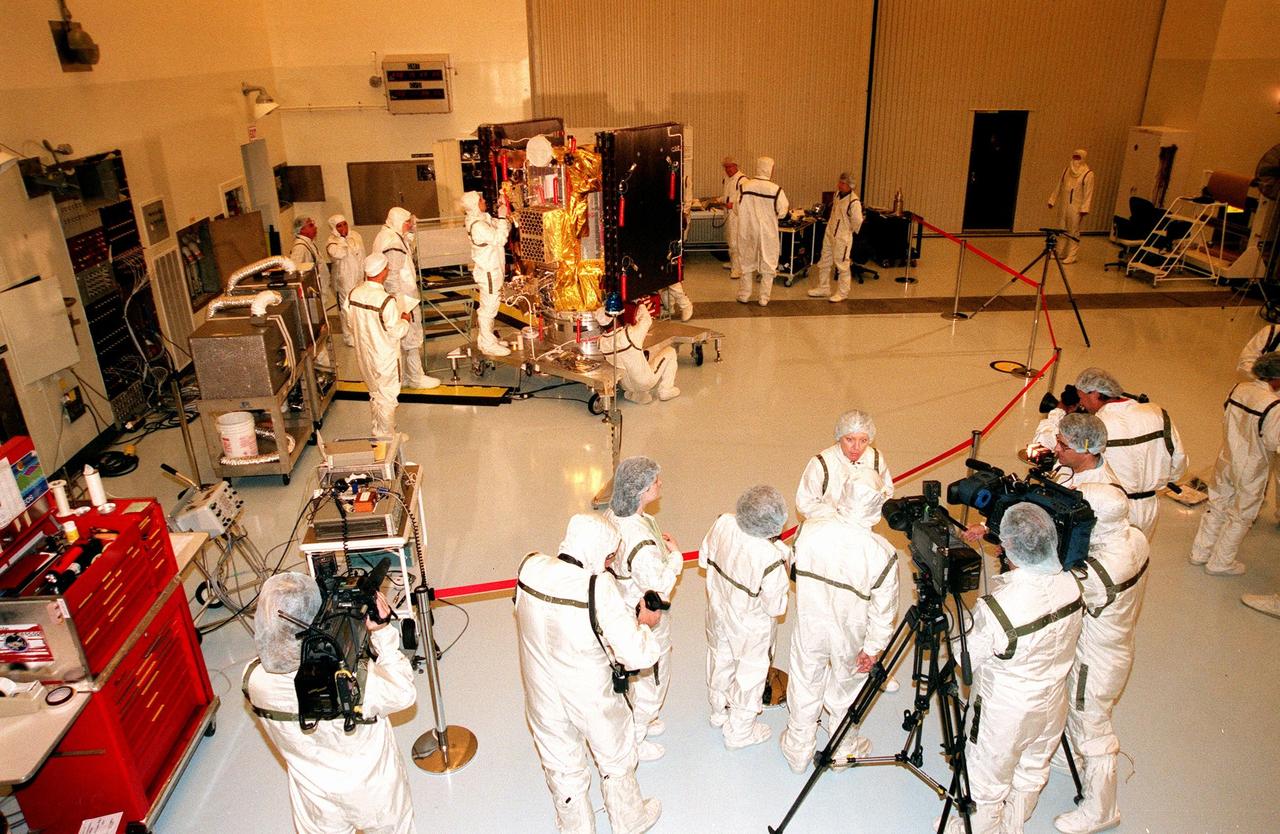 KENNEDY SPACE CENTER, FLA. -- In the Payload Hazardous Servicing Facility, the media (below), dressed in "bunny" suits, learn about Deep Space 1 from Leslie Livesay (facing cameras), Deep Space 1 spacecraft manager from the Jet Propulsion Laboratory. In the background, KSC workers place insulating blankets on Deep Space 1. The first flight in NASA's New Millennium Program, Deep Space 1 is designed to validate 12 new technologies for scientific space missions of the next century. Onboard experiments include an ion propulsion engine and software that tracks celestial bodies so the spacecraft can make its own navigation decisions without the intervention of ground controllers. Deep Space 1 will complete most of its mission objectives within the first two months, but may also do a flyby of a near-Earth asteroid, 1992 KD, in July 1999. Deep Space 1 will be launched aboard a Boeing Delta 7326 rocket from Launch Pad 17A, Cape Canaveral Air Station, in October. Delta II rockets are medium capacity expendable launch vehicles derived from the Delta family of rockets built and launched since 1960. Since then there have been more than 245 Delta launches