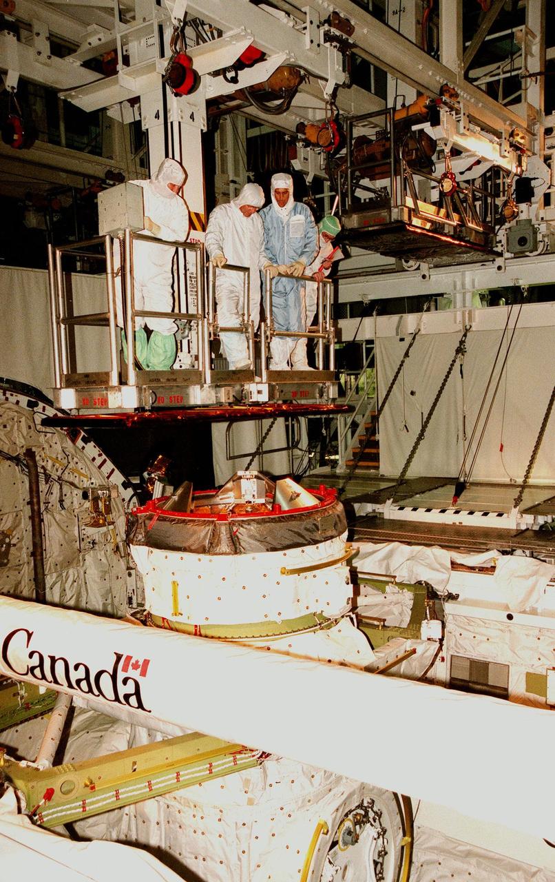 KENNEDY SPACE CENTER, FLA. -- As the bucket operator (left) lowers them into the open payload bay of the orbiter Endeavour, STS-88 Mission Specialists Jerry L. Ross (second from left) and James H. Newman (second from right) do a sharp-edge inspection. At their right is Wayne Wedlake, with United Space Alliance at Johnson Space Center. Below them is the Orbiter Docking System, the remote manipulator system arm and a tunnel into the payload bay. The STS-88 crew members are participating in a Crew Equipment Interface Test (CEIT), familiarizing themselves with the orbiter's midbody and crew compartments. Targeted for liftoff on Dec. 3, 1998, STS-88 will be the first Space Shuttle launch for assembly of the International Space Station (ISS). The primary payload is the Unity connecting module which will be mated to the Russian-built Zarya control module, expected to be already on orbit after a November launch from Russia. After the mating, Ross and Newman are scheduled to perform three spacewalks to connect power, data and utility lines and install exterior equipment. The first major U.S.-built component of ISS, Unity will serve as a connecting passageway to living and working areas of the space station. Unity has two attached pressurized mating adapters (PMAs) and one stowage rack installed inside. PMA-1 provides the permanent connection point between Unity and Zarya; PMA-2 will serve as a Space Shuttle docking port. Zarya is a self-supporting active vehicle, providing propulsive control capability and power during the early assembly stages. It also has fuel storage capability