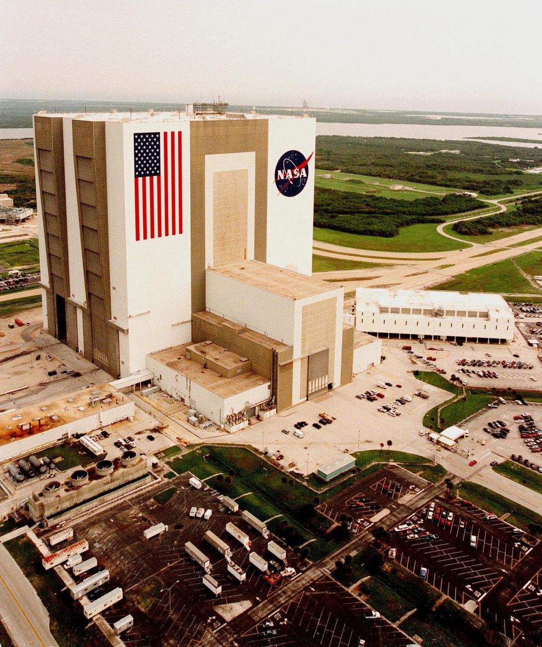 KENNEDY SPACE CENTER, FLA. -- The Vehicle Assembly Building (VAB) in the Launch Complex 39 area wears a new coat of paint, along with newly painted American flag and NASA logo. The improved look was finished in time to honor NASA's 40th anniversary on Oct. 1. In order to do the job, workers were suspended on platforms from the top of the 525-foot-high VAB. One of the world's largest buildings by volume, the VAB is the last stop for the Shuttle before rollout to the launch pad. Integration and stacking of the complete Space Shuttle vehicle (orbiter, two solid rocket boosters and the external tank) takes place in High Bays 1 or 3. To the right of the VAB is the Launch Control Center. Each of its four firing rooms are equipped with automated, computer-controlled Launch Processing System (LPS) for monitoring and controlling Shuttle assembly, checkout and launch operations, as well as work order control and scheduling. Banana Creek is visible behind and to the right of the VAB