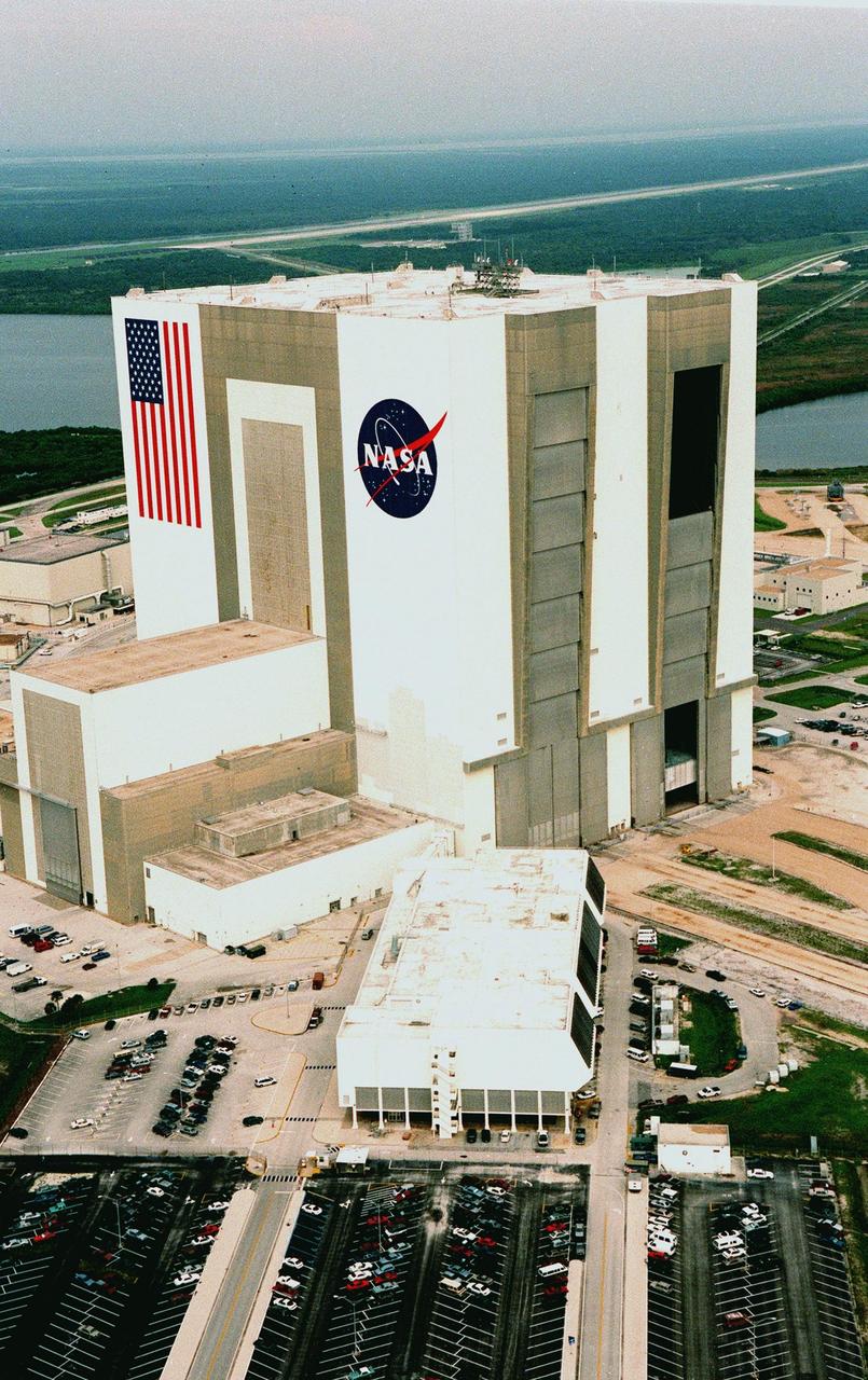 KENNEDY SPACE CENTER, FLA. -- Looking northwest, the Vehicle Assembly Building (VAB) in the Launch Complex 39 area of KSC can be seen with its new coat of paint, along with newly painted American flag and NASA logo. The improved look was finished in time to honor NASA's 40th anniversary on Oct. 1. In order to do the job, workers were suspended on platforms from the top of the 525-foot-high VAB. One of the world's largest buildings by volume, the VAB is the last stop for the Shuttle before rollout to the launch pad. Integration and stacking of the complete Space Shuttle vehicle (orbiter, two solid rocket boosters and the external tank) takes place in High Bays 1 or 3. The High Bay doors (shown partially open), four in all, are 456 feet high. The low-door section, 114 feet high, has four panels that move horizontally. The upper section, 342 feet high, has seven panels that move vertically. It takes about 45 minutes to open all panels. Beyond the VAB is the Shuttle Landing Facility (SLF) and Merritt Island National Wildlife Refuge. The SLF is used for end-of-mission orbiter landings, and also military and civilian cargo carriers, astronauts' T-38 trainers, Shuttle Training Aircraft, and helicopters