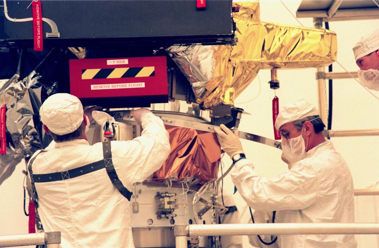 KENNEDY SPACE CENTER, FLA. -- Workers at the Defense Satellite Communications System Processing Facility (DPF), Cape Canaveral Air Station (CCAS), attach a strap during installation of the ion propulsion engine on Deep Space 1. The first flight in NASA's New Millennium Program, Deep Space 1 is designed to validate 12 new technologies for scientific space missions of the next century, including the engine. Propelled by the gas xenon, the engine is being flight-tested for future deep space and Earth-orbiting missions. Deceptively powerful, the ion drive emits only an eerie blue glow as ionized atoms of xenon are pushed out of the engine. While slow to pick up speed, over the long haul it can deliver 10 times as much thrust per pound of fuel as liquid or solid fuel rockets. Other onboard experiments include software that tracks celestial bodies so the spacecraft can make its own navigation decisions without the intervention of ground controllers. Deep Space 1 will complete most of its mission objectives within the first two months, but will also do a flyby of a near-Earth asteroid, 1992 KD, in July 1999. Deep Space 1 will be launched aboard a Boeing Delta 7326 rocket from Launch Pad 17A, CCAS, in October