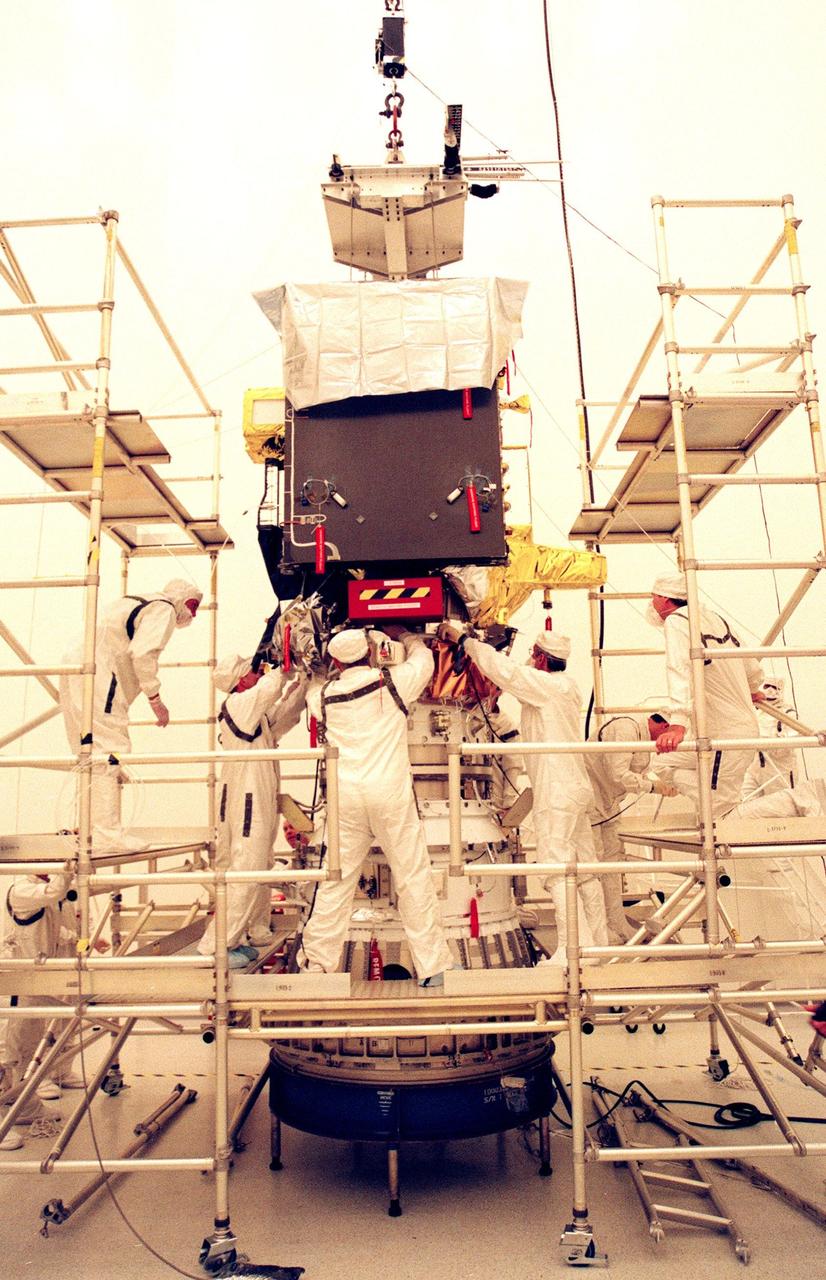 KENNEDY SPACE CENTER, FLA. -- Workers at the Defense Satellite Communications System Processing Facility (DPF), Cape Canaveral Air Station (CCAS), make adjustments while installing the ion propulsion engine on Deep Space 1. The first flight in NASA's New Millennium Program, Deep Space 1 is designed to validate 12 new technologies for scientific space missions of the next century, including the engine. Propelled by the gas xenon, the engine is being flight-tested for future deep space and Earth-orbiting missions. Deceptively powerful, the ion drive emits only an eerie blue glow as ionized atoms of xenon are pushed out of the engine. While slow to pick up speed, over the long haul it can deliver 10 times as much thrust per pound of fuel as liquid or solid fuel rockets. Other onboard experiments include software that tracks celestial bodies so the spacecraft can make its own navigation decisions without the intervention of ground controllers. Deep Space 1 will complete most of its mission objectives within the first two months, but will also do a flyby of a near-Earth asteroid, 1992 KD, in July 1999. Deep Space 1 will be launched aboard a Boeing Delta 7326 rocket from Launch Pad 17A, CCAS, in October