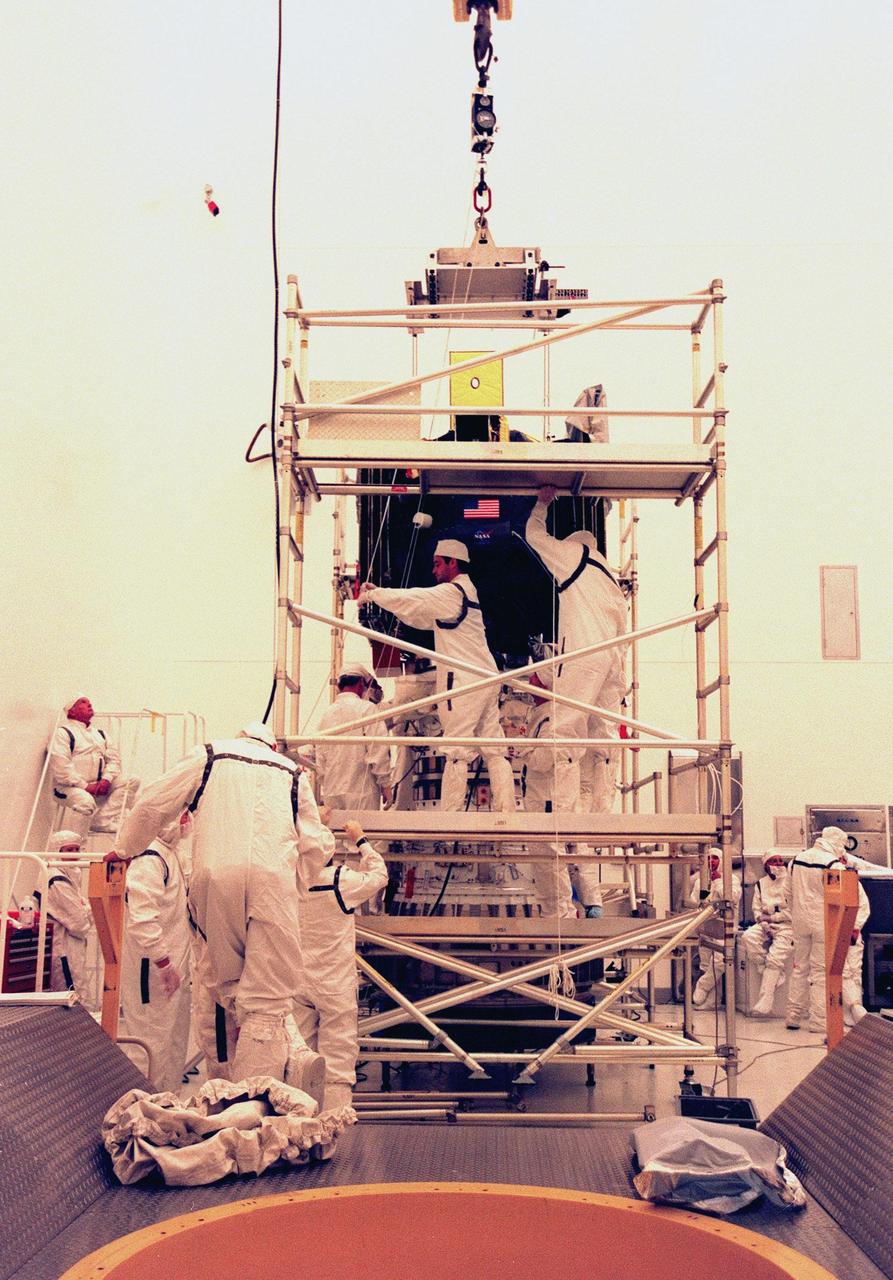 KENNEDY SPACE CENTER, FLA. -- Workers at the Defense Satellite Communications System Processing Facility (DPF), Cape Canaveral Air Station (CCAS), maneuver the ion propulsion engine into place before installation on Deep Space 1. The first flight in NASA's New Millennium Program, Deep Space 1 is designed to validate 12 new technologies for scientific space missions of the next century, including the engine. Propelled by the gas xenon, the engine is being flight-tested for future deep space and Earth-orbiting missions. Deceptively powerful, the ion drive emits only an eerie blue glow as ionized atoms of xenon are pushed out of the engine. While slow to pick up speed, over the long haul it can deliver 10 times as much thrust per pound of fuel as liquid or solid fuel rockets. Other onboard experiments include software that tracks celestial bodies so the spacecraft can make its own navigation decisions without the intervention of ground controllers. Deep Space 1 will complete most of its mission objectives within the first two months, but will also do a flyby of a near-Earth asteroid, 1992 KD, in July 1999. Deep Space 1 will be launched aboard a Boeing Delta 7326 rocket from Launch Pad 17A, CCAS, in October