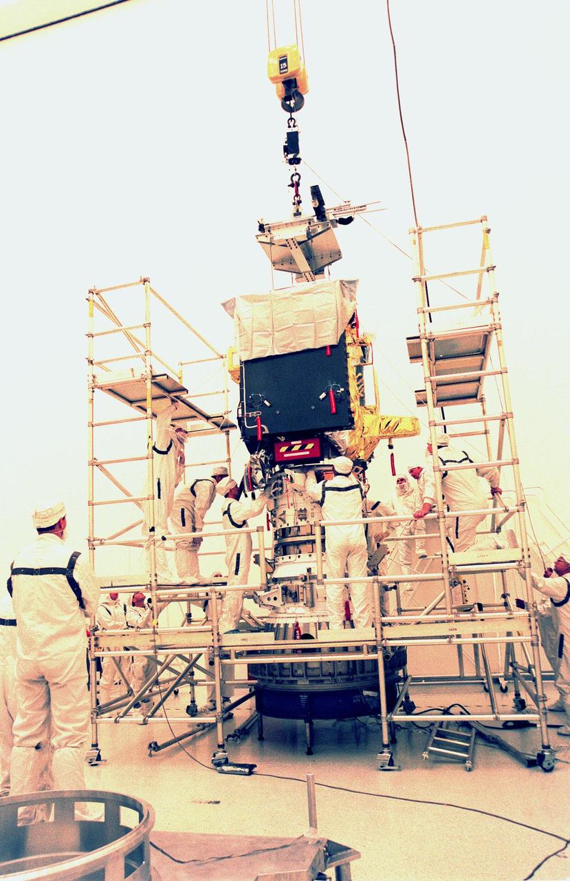 KENNEDY SPACE CENTER, FLA. -- Workers in the Defense Satellite Communications Systems Processing Facility (DPF) at Cape Canaveral Air Station (CCAS) make adjustments while installing the ion propulsion engine on Deep Space 1. The first flight in NASA's New Millennium Program, Deep Space 1 is designed to validate 12 new technologies for scientific space missions of the next century, including the engine. Propelled by the gas xenon, the engine is being flight-tested for future deep space and Earth-orbiting missions. Deceptively powerful, the ion drive emits only an eerie blue glow as ionized atoms of xenon are pushed out of the engine. While slow to pick up speed, over the long haul it can deliver 10 times as much thrust per pound of fuel as liquid or solid fuel rockets. Other onboard experiments include software that tracks celestial bodies so the spacecraft can make its own navigation decisions without the intervention of ground controllers. Deep Space 1 will complete most of its mission objectives within the first two months, but will also do a flyby of a near-Earth asteroid, 1992 KD, in July 1999. Deep Space 1 will be launched Oct. 25 aboard a Boeing Delta 7326 rocket from Launch Pad 17A, CCAS