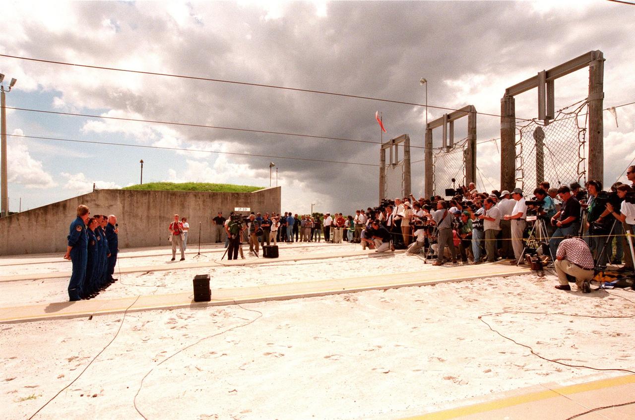 In front of the bunker near Launch Pad 39-B, the STS-95 crew members (at left) respond to questions about the mission and training from 106 reporters and photographers during a brief break from the Terminal Countdown Demonstration Test (TCDT). From left they are Mission Specialist Scott E. Parazynski, Mission Specialist Stephen K. Robinson, who also serves as Payload Commander, Pilot Steven W. Lindsey, Mission Commander Curtis L. Brown, Mission Specialist Pedro Duque of Spain, representing the European Space Agency (ESA), Payload Specialist Chiaki Mukai, representing the National Space Development Agency of Japan (NASDA), and Payload Specialist John H. Glenn Jr., senator from Ohio, holding a microphone. The crew were at the pad for emergency egress training after the break. Above them are the slidewires leading to the catch nets for the baskets that are used in emergency egress. The TCDT also involves mission familiarization activities and a simulated main engine cut-off exercise. The STS-95 mission, targeted for liftoff on Oct. 29, includes research payloads such as the Spartan solar-observing deployable spacecraft, the Hubble Space Telescope Orbital Systems Test Platform, the International Extreme Ultraviolet Hitchhiker, as well as the SPACEHAB single module with experiments on space flight and the aging process. Following the TCDT, the crew will be returning to Houston for final flight preparations