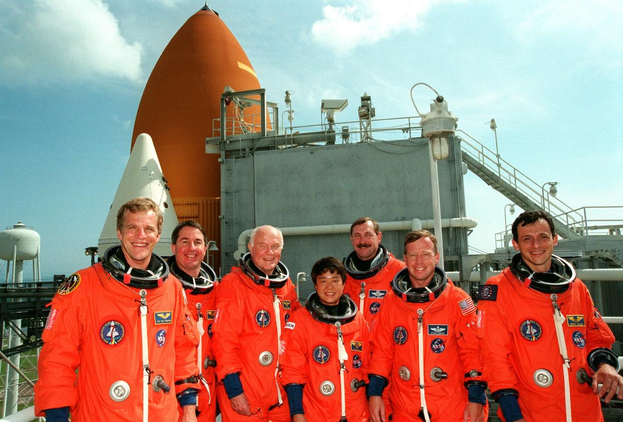 On Launch Pad 39B, the STS-95 crew pose after successfully completing a pre-launch countdown exercise on Space Shuttle Discovery. Standing from left to right are Mission Specialist Scott E. Parazynski, Mission Specialist Stephen K. Robinson, Payload Specialist John H. Glenn Jr., senator from Ohio, Payload Specialist Chiaki Mukai (M.D., Ph.D.), representing the National Space Development Agency in Japan (NASDA), Mission Commander Curtis L. Brown, Pilot Steven W. Lindsey, and Mission Specialist Pedro Duque of Spain, representing the European Space Agency (ESA). In the background can be seen one of the solid rocket boosters and the external tank. The STS-95 crew are at KSC to participate in the Terminal Countdown Demonstration Test (TCDT) which includes mission familiarization activities, emergency egress training, and a simulated main engine cutoff. The STS-95 mission, targeted for liftoff on Oct. 29, includes research payloads such as the Spartan solar-observing deployable spacecraft, the Hubble Space Telescope Orbital Systems Test Platform, the International Extreme Ultraviolet Hitchhiker, as well as the SPACEHAB single module with experiments on space flight and the aging process. Following the TCDT, the crew will be returning to Houston for final flight preparations
