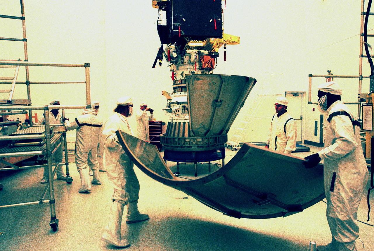 KENNEDY SPACE CENTER, FLA. -- Workers in the Defense Satellite Communication Systems Processing Facility (DPF), Cape Canaveral Air Station (CCAS), move to the workstand the second conical section leaf of the payload transportation container for Deep Space 1. The first flight in NASA's New Millennium Program, Deep Space 1 is designed to validate 12 new technologies for scientific space missions of the next century, including the engine. Propelled by the gas xenon, the engine is being flight-tested for future deep space and Earth-orbiting missions. Deceptively powerful, the ion drive emits only an eerie blue glow as ionized atoms of xenon are pushed out of the engine. While slow to pick up speed, over the long haul it can deliver 10 times as much thrust per pound of fuel as liquid or solid fuel rockets. Other onboard experiments include software that tracks celestial bodies so the spacecraft can make its own navigation decisions without the intervention of ground controllers. Deep Space 1 will complete most of its mission objectives within the first two months, but will also do a flyby of a near-Earth asteroid, 1992 KD, in July 1999. Deep Space 1 will be launched aboard a Boeing Delta 7326 rocket from Launch Pad 17A, CCAS