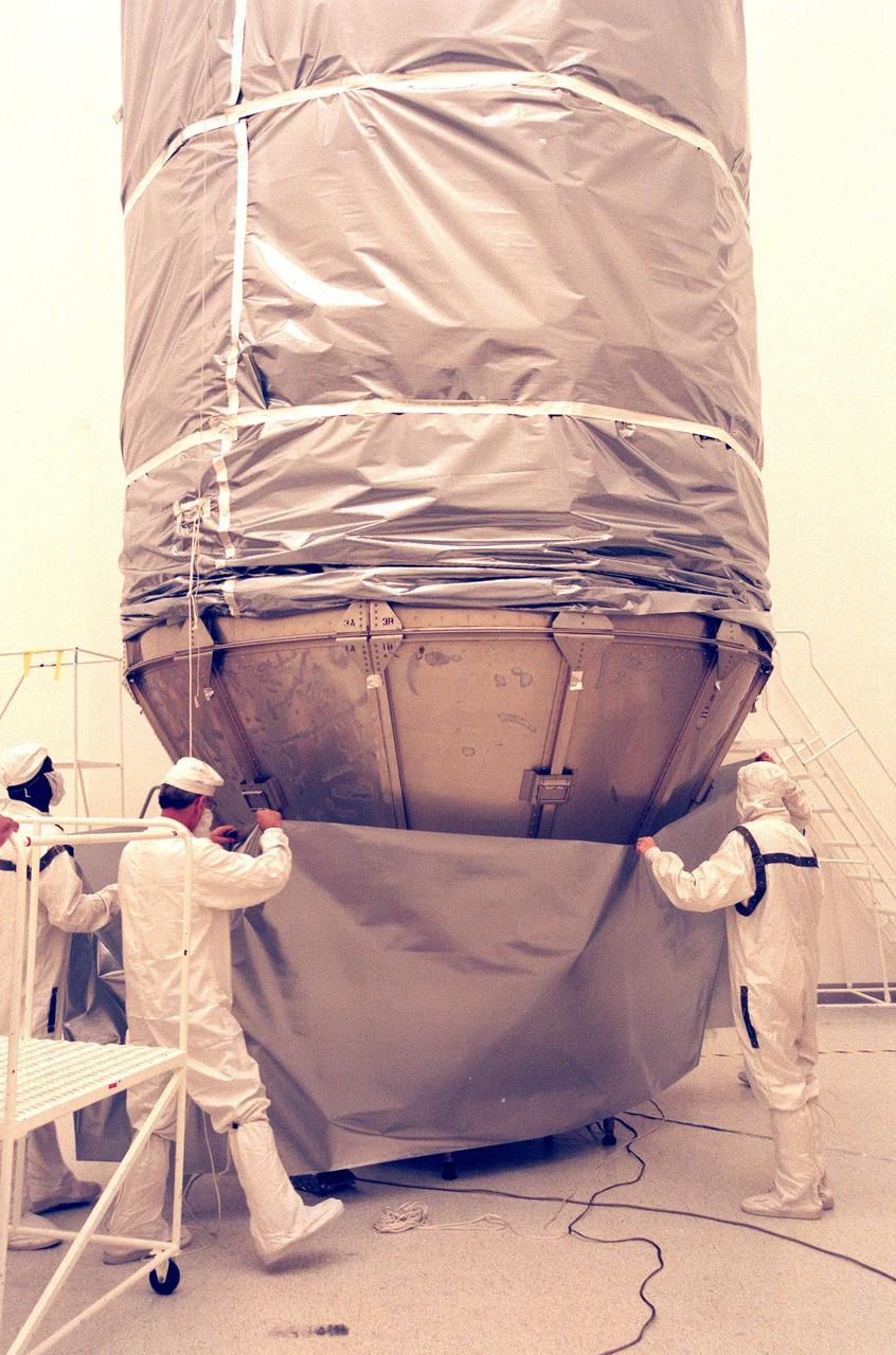 KENNEDY SPACE CENTER, FLA. -- In the Defense Satellite Communications Systems Processing Facility (DPF), Cape Canaveral Air Station (CCAS), workers place an anti-static blanket over the lower portion of Deep Space 1, to protect the spacecraft during transport to the launch pad. The first flight in NASA's New Millennium Program, Deep Space 1 is designed to validate 12 new technologies for scientific space missions of the next century, including the engine. Propelled by the gas xenon, the engine is being flight-tested for future deep space and Earth-orbiting missions. Deceptively powerful, the ion drive emits only an eerie blue glow as ionized atoms of xenon are pushed out of the engine. While slow to pick up speed, over the long haul it can deliver 10 times as much thrust per pound of fuel as liquid or solid fuel rockets. Other onboard experiments include software that tracks celestial bodies so the spacecraft can make its own navigation decisions without the intervention of ground controllers. Deep Space 1 will complete most of its mission objectives within the first two months, but will also do a flyby of a near-Earth asteroid, 1992 KD, in July 1999. Deep Space 1 will be launched aboard a Boeing Delta 7326 rocket from Launch Pad 17A, CCAS