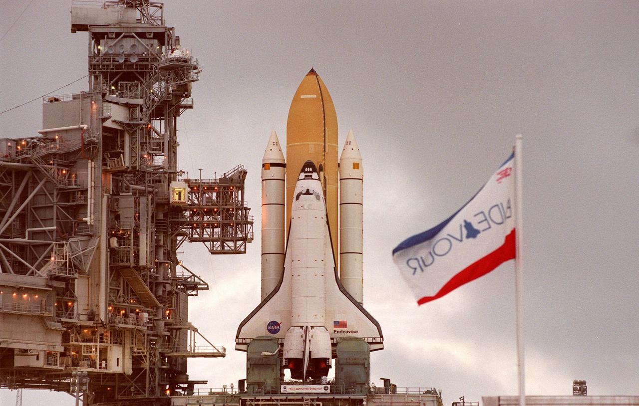 KENNEDY SPACE CENTER,  Fla. -- Space Shuttle Endeavour arrives at Launch Pad 39A in the dim early morning light, atop the mobile launcher platform and crawler transporter, after rollout from the Vehicle Assembly Building. The flag identifying the Shuttle (at right) waves slightly from the wind. At left are the Fixed Service Structure and Rotating Service Structure. While at the pad, the orbiter, external tank and solid rocket boosters will undergo final preparations for the STS-88 launch targeted for Dec. 3, 1998. Mission STS-88 is the first U.S. flight for the assembly of the International Space Station and will carry the Unity connecting module. While on orbit, the flight crew will deploy Unity from the payload bay and connect it to the Russian-built Zarya control module which will be in orbit at that time. Unity will be the main connecting point for later U.S. station modules and components. More than 40 launches are planned over five years involving the resources and expertise of 16 cooperating nations. Comprising the STS-88 crew are Commander Robert D. Cabana, Pilot Frederick W. "Rick" Sturckow, Mission Specialists Nancy J. Currie, Jerry L. Ross, James H. Newman and Russian cosmonaut Sergei Konstantinovich Krikalev. Ross and Newman will make three spacewalks to connect power, data and utility lines and install exterior equipment