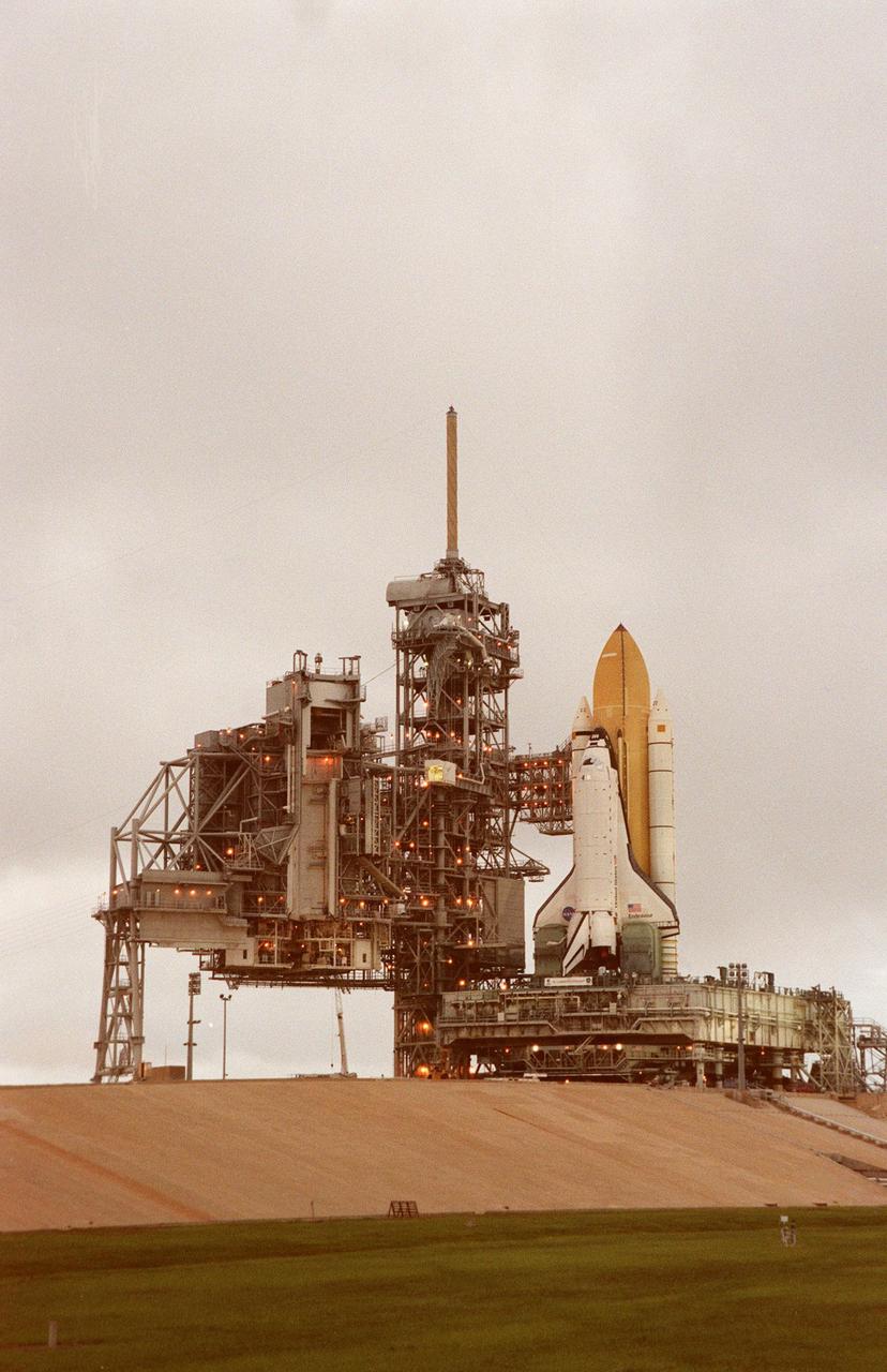 KENNEDY SPACE CENTER,  Fla. -- In the cloud-dimmed light of early morning, Space Shuttle Endeavour sits in place at Launch Pad 39A , atop the mobile launcher platform and crawler transporter, after rollout from the Vehicle Assembly Building. At its left are the Rotating Service Structure and Fixed Service Structure with the orbiter access arm extended. The access arm swings out to the orbiter crew compartment hatch to allow personnel to enter the crew compartment. At its outer end is the white room, an environmental chamber, that mates with the orbiter. While at the pad, the orbiter, external tank and solid rocket boosters will undergo final preparations for the STS-88 launch targeted for Dec. 3, 1998. Mission STS-88 is the first U.S. flight for the assembly of the International Space Station and will carry the Unity connecting module. While on orbit, the flight crew will deploy Unity from the payload bay and connect it to the Russian-built Zarya control module which will be in orbit at that time. Unity will be the main connecting point for later U.S. station modules and components. More than 40 launches are planned over five years involving the resources and expertise of 16 cooperating nations. Comprising the STS-88 crew are Commander Robert D. Cabana, Pilot Frederick W. "Rick" Sturckow, Mission Specialists Nancy J. Currie, Jerry L. Ross, James H. Newman and Russian cosmonaut Sergei Konstantinovich Krikalev. Ross and Newman will make three spacewalks to connect power, data and utility lines and install exterior equipment