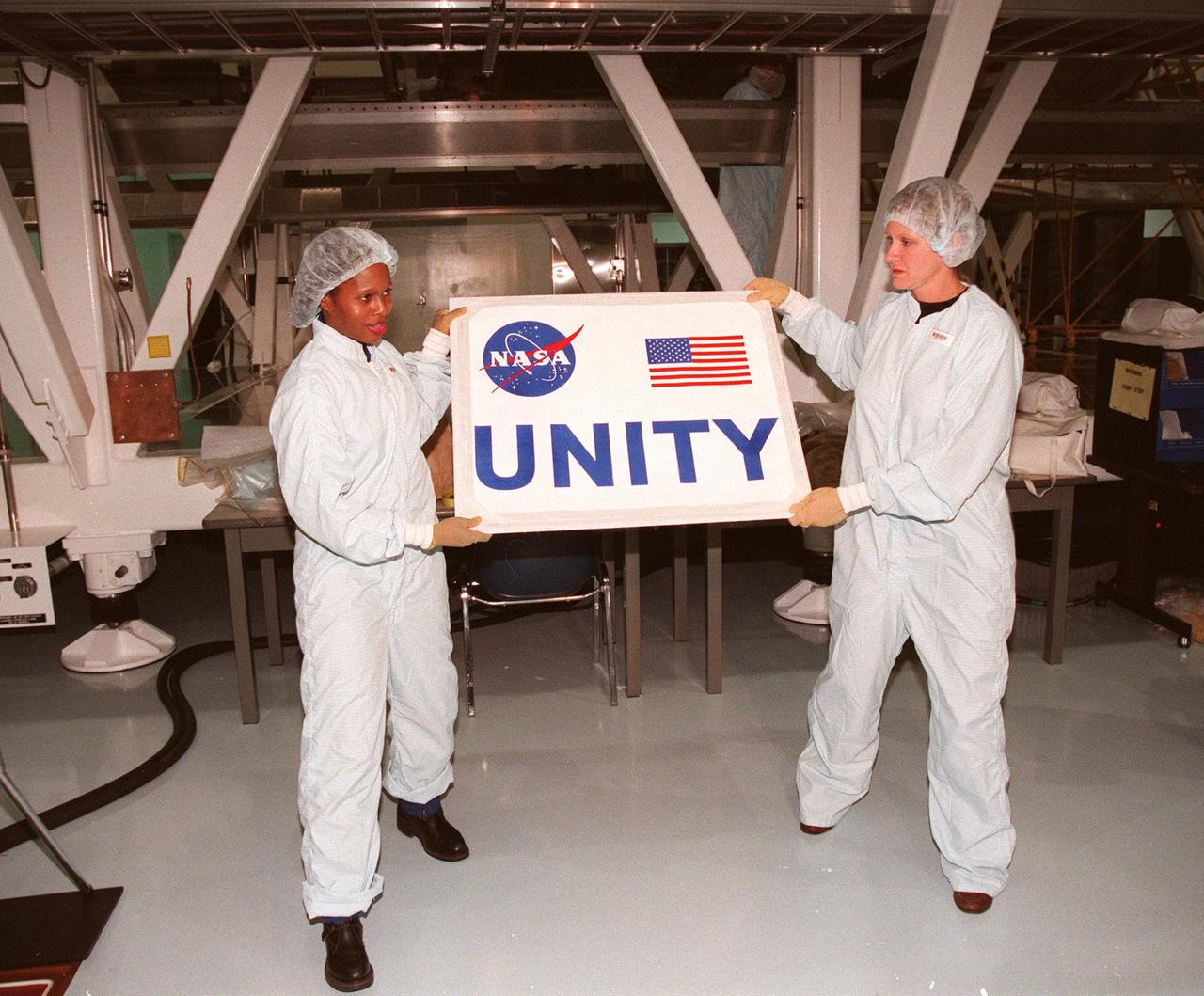 In the Space Station Processing Facility, holding the nameplate for the Unity connecting module are (left) Joan Higginbotham, with the Astronaut Office Computer Support Branch, and (right) Nancy Tolliver, with Boeing-Huntsville. Part of the International Space Station, Unity was expected to be transported to Launch Pad 39A on Oct. 26 for launch aboard Space Shuttle Endeavour on Mission STS-88 in December. The Unity is a connecting passageway to the living and working areas of ISS. While on orbit, the flight crew will deploy Unity from the payload bay and attach Unity to the Russian-built Zarya control module which will be in orbit at that time