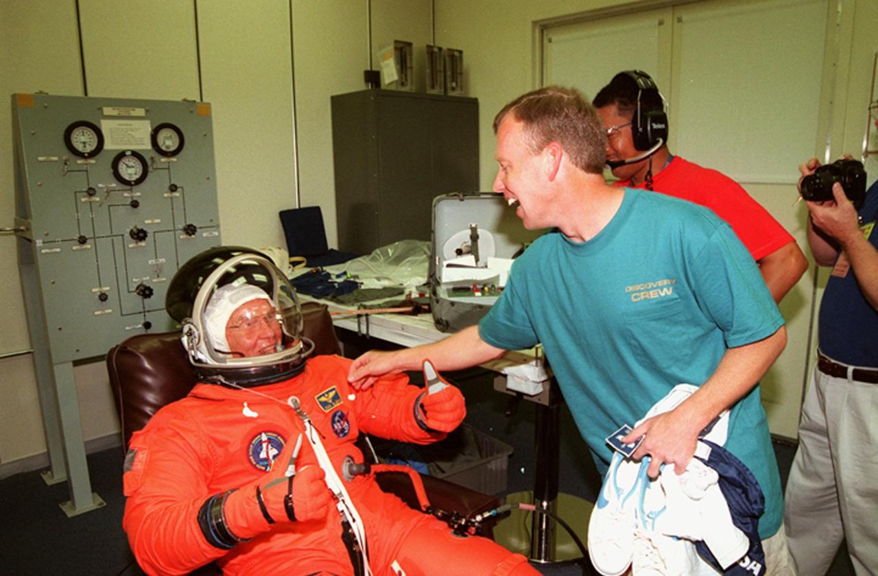 KENNEDY SPACE CENTER, FLA. -- In the Operations and Checkout Building, STS-95 Pilot Steven W. Lindsey (right) reaches playfully for the name tag on the flight suit of Payload Specialist John H. Glenn Jr., senator from Ohio, seated in the chair. The STS-95 crew were conducting flight crew equipment fit checks prior to launch on Oct. 29. STS-95 is expected to launch at 2 p.m. EST on Oct. 29, last 8 days, 21 hours and 49 minutes, and land at 11:49 a.m. EST on Nov. 7