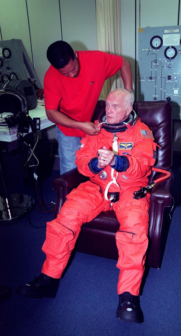 In the Operations and Checkout Building, suit technician George Brittingham helps STS-95 Payload Specialist John H. Glenn Jr., senator from Ohio, with his suit. The STS-95 crew were conducting flight crew equipment fit checks prior to launch on Oct. 29. STS-95 is expected to launch at 2 p.m. EST on Oct. 29, last 8 days, 21 hours and 49 minutes, and land at 11:49 a.m. EST on Nov. 7