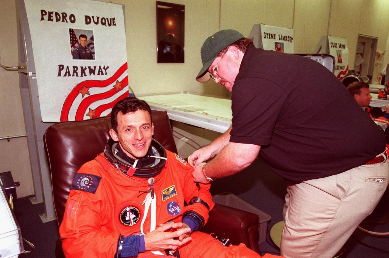 STS-95 Mission Specialist Pedro Duque of Spain, with the European Space Agency, is helped with his flight suit by suit tech Tommy McDonald in the Operations and Checkout Building. The final fitting takes place prior to the crew walkout and transport to Launch Pad 39B. Targeted for launch at 2 p.m. EST on Oct. 29, the mission is expected to last 8 days, 21 hours and 49 minutes, and return to KSC at 11:49 a.m. EST on Nov. 7. The STS-95 mission includes research payloads such as the Spartan solar-observing deployable spacecraft, the Hubble Space Telescope Orbital Systems Test Platform, the International Extreme Ultraviolet Hitchhiker, as well as the SPACEHAB single module with experiments on space flight and the aging process
