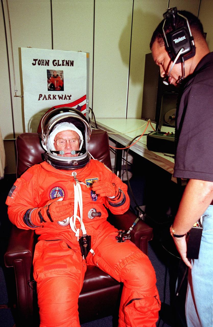 STS-95 Payload Specialist John H. Glenn Jr., senator from Ohio, tests the fitting of his flight suit in the Operations and Checkout Building while suit tech George Brittingham watches. The final fitting takes place prior to the crew walkout and transport to Launch Pad 39B. Targeted for launch at 2 p.m. EST on Oct. 29, the mission is expected to last 8 days, 21 hours and 49 minutes, and return to KSC at 11:49 a.m. EST on Nov. 7. The STS-95 mission includes research payloads such as the Spartan solar-observing deployable spacecraft, the Hubble Space Telescope Orbital Systems Test Platform, the International Extreme Ultraviolet Hitchhiker, as well as the SPACEHAB single module with experiments on space flight and the aging process
