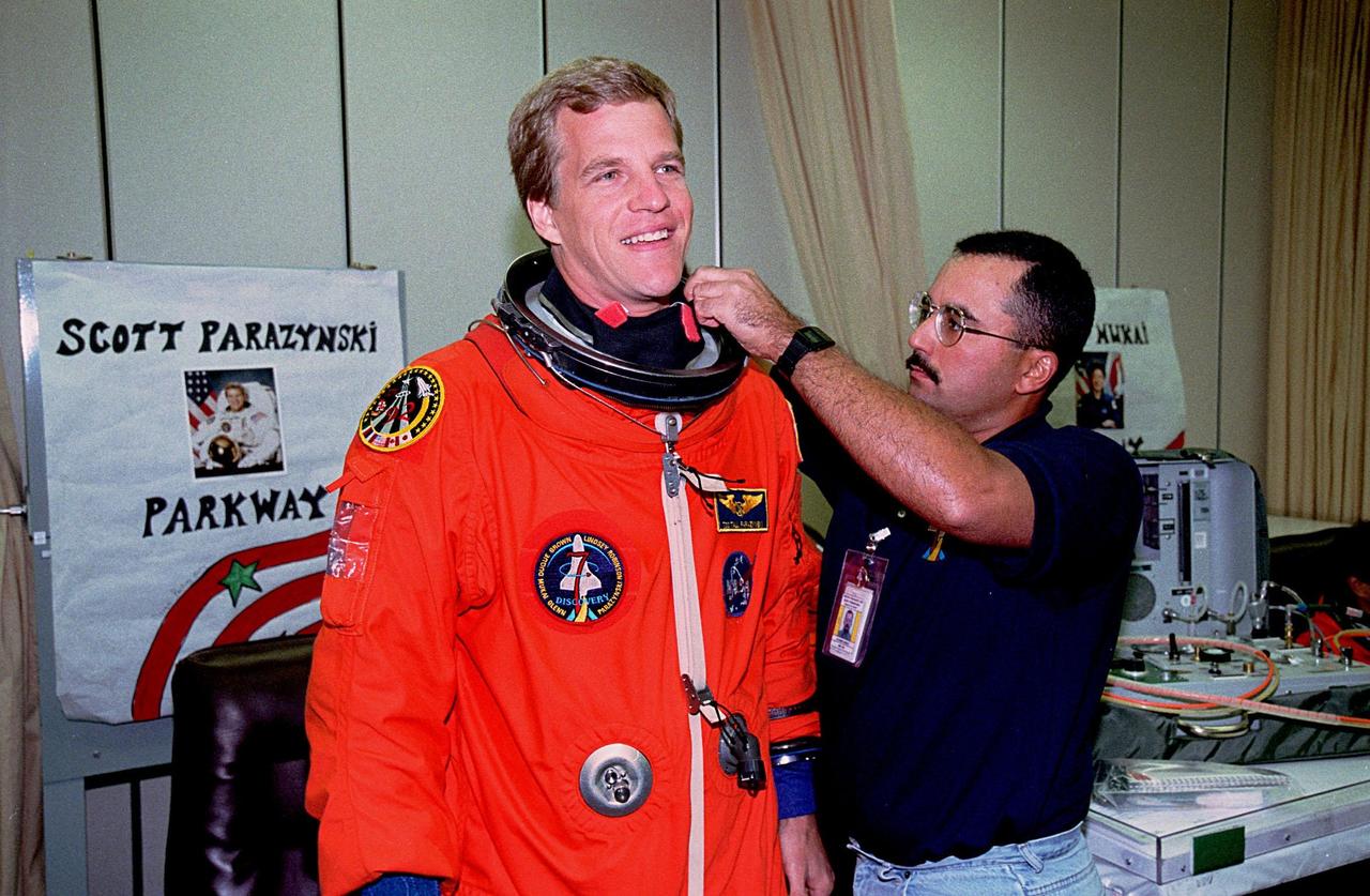 STS-95 Mission Specialist Scott E. Parazynski gets help with his flight suit in the Operations and Checkout Building from a suit technician George Brittingham. The final fitting takes place prior to the crew walkout and transport to Launch Pad 39B. Targeted for launch at 2 p.m. EST on Oct. 29, the mission is expected to last 8 days, 21 hours and 49 minutes, and return to KSC at 11:49 a.m. EST on Nov. 7. The STS-95 mission includes research payloads such as the Spartan solar-observing deployable spacecraft, the Hubble Space Telescope Orbital Systems Test Platform, the International Extreme Ultraviolet Hitchhiker, as well as the SPACEHAB single module with experiments on space flight and the aging process