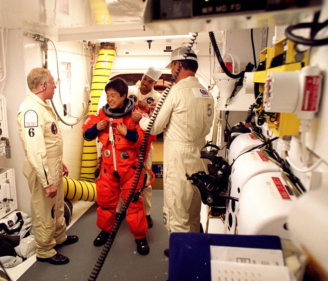 In the environmental chamber known as the white room, STS-95 Payload Specialist Chiaki Mukai, with the National Space Development Agency of Japan (NASDA), is prepared by closeout room crew members Danny Wyatt (left), Carlous Gillis (behind her) and Dave Law (right) for entry into the Space Shuttle Discovery for her second flight into space. The STS-95 mission, targeted for launch at 2 p.m. EST on Oct. 29, is expected to last 8 days, 21 hours and 49 minutes, and return to KSC at 11:49 a.m. EST on Nov. 7