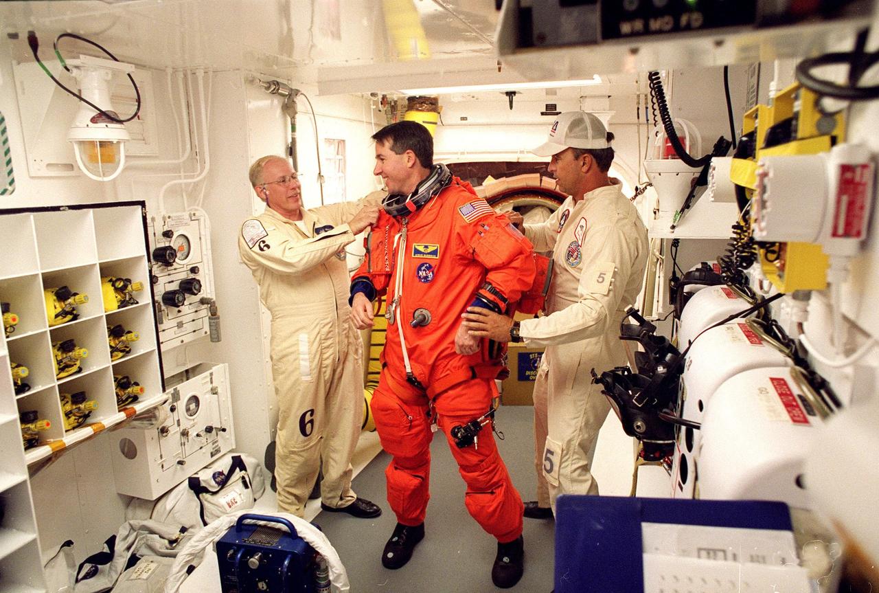 In the environmental chamber known as the white room, STS-95 Mission Specialist Stephen K. Robinson is prepared by closeout room crew members (left) Danny Wyatt and Dave Law (right) for entry into the Space Shuttle Discovery for his second flight into space. The STS-95 mission, targeted for launch at 2 p.m. EST on Oct. 29, is expected to last 8 days, 21 hours and 49 minutes, and return to KSC at 11:49 a.m. EST on Nov. 7