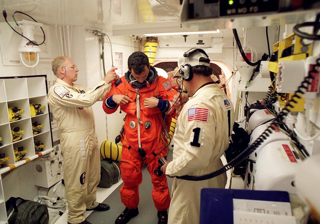 In the environmental chamber known as the white room, STS-95 Mission Specialist Pedro Duque of Spain, with the European Space Agency, is prepared by closeout room crew members Danny Wyatt (left) and Travis Thompson (right) for entry into the Space Shuttle Discovery for his first flight into space. The STS-95 mission, targeted for launch at 2 p.m. EST on Oct. 29, is expected to last 8 days, 21 hours and 49 minutes, and return to KSC at 11:49 a.m. EST on Nov. 7