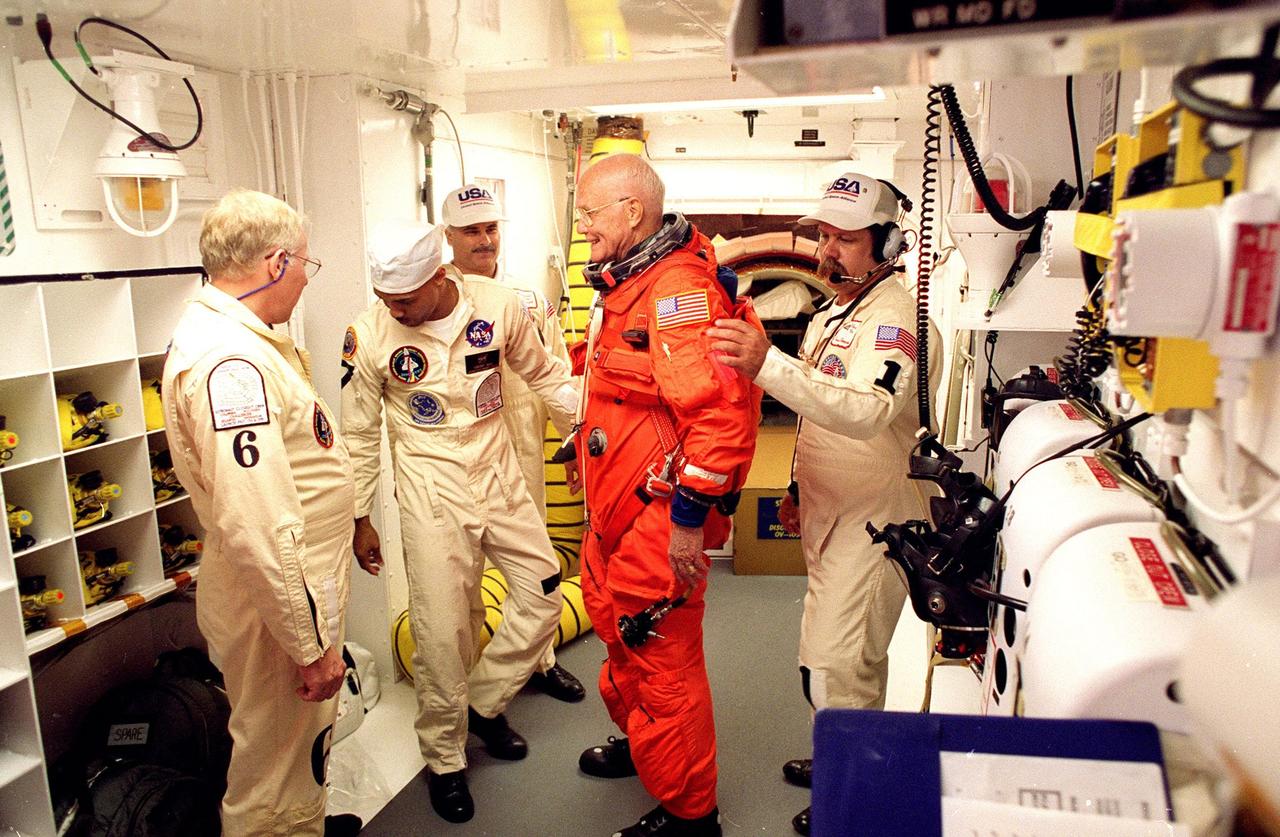 In the environmental chamber known as the white room, STS-95 Payload Specialist John H. Glenn Jr., senator from Ohio, is prepared by closeout room crew members Danny Wyatt (left to right), Carlous Gillis, Jim Kelly and Travis Thompson for entry into the Space Shuttle Discovery for his second flight into space after 36 years. The STS-95 mission, targeted for launch at 2 p.m. EST on Oct. 29, is expected to last 8 days, 21 hours and 49 minutes, and return to KSC at 11:49 a.m. EST on Nov. 7