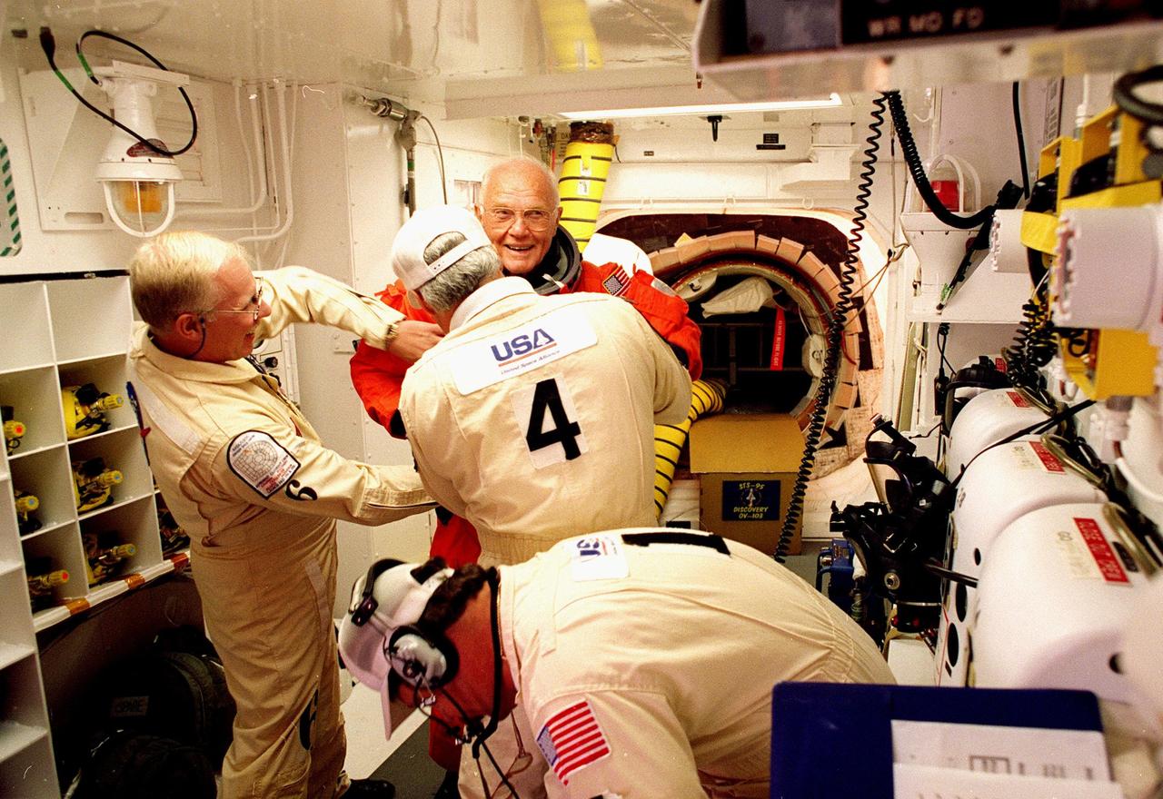 In the environmental chamber known as the white room, an eager STS-95 Payload Specialist John H. Glenn Jr., senator from Ohio, has his flight suit checked by closeout room crew members Danny Wyatt (left to right), Chris Meinert and Travis Thompson (foreground) for entry into the Space Shuttle Discovery for his second flight into space after 36 years. The STS-95 mission, targeted for launch at 2 p.m. EST on Oct. 29, is expected to last 8 days, 21 hours and 49 minutes, and return to KSC at 11:49 a.m. EST on Nov. 7