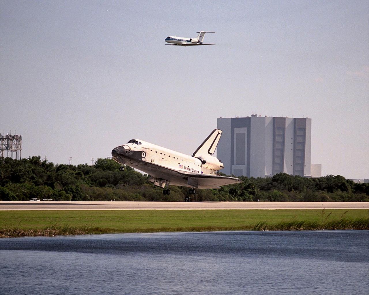 Viewed across the creek bordering runway 33, orbiter Discovery prepares to touch down at the Shuttle Landing Facility after a successful mission of nearly nine days and 3.6 million miles. Flying above it is the Shuttle Training Aircraft. Main gear touchdown was at 12:04 p.m. EST, landing on orbit 135. In the background, right, is the Vehicle Assembly Building. The STS-95 crew consists of Mission Commander Curtis L. Brown Jr.; Pilot Steven W. Lindsey; Mission Specialist Scott E. Parazynski; Mission Specialist Stephen K. Robinson; Payload Specialist John H. Glenn Jr., senator from Ohio; Mission Specialist Pedro Duque, with the European Space Agency (ESA); and Payload Specialist Chiaki Mukai, with the National Space Development Agency of Japan (NASDA). The mission included research payloads such as the Spartan solar-observing deployable spacecraft, the Hubble Space Telescope Orbital Systems Test Platform, the International Extreme Ultraviolet Hitchhiker, as well as the SPACEHAB single module with experiments on space flight and the aging process