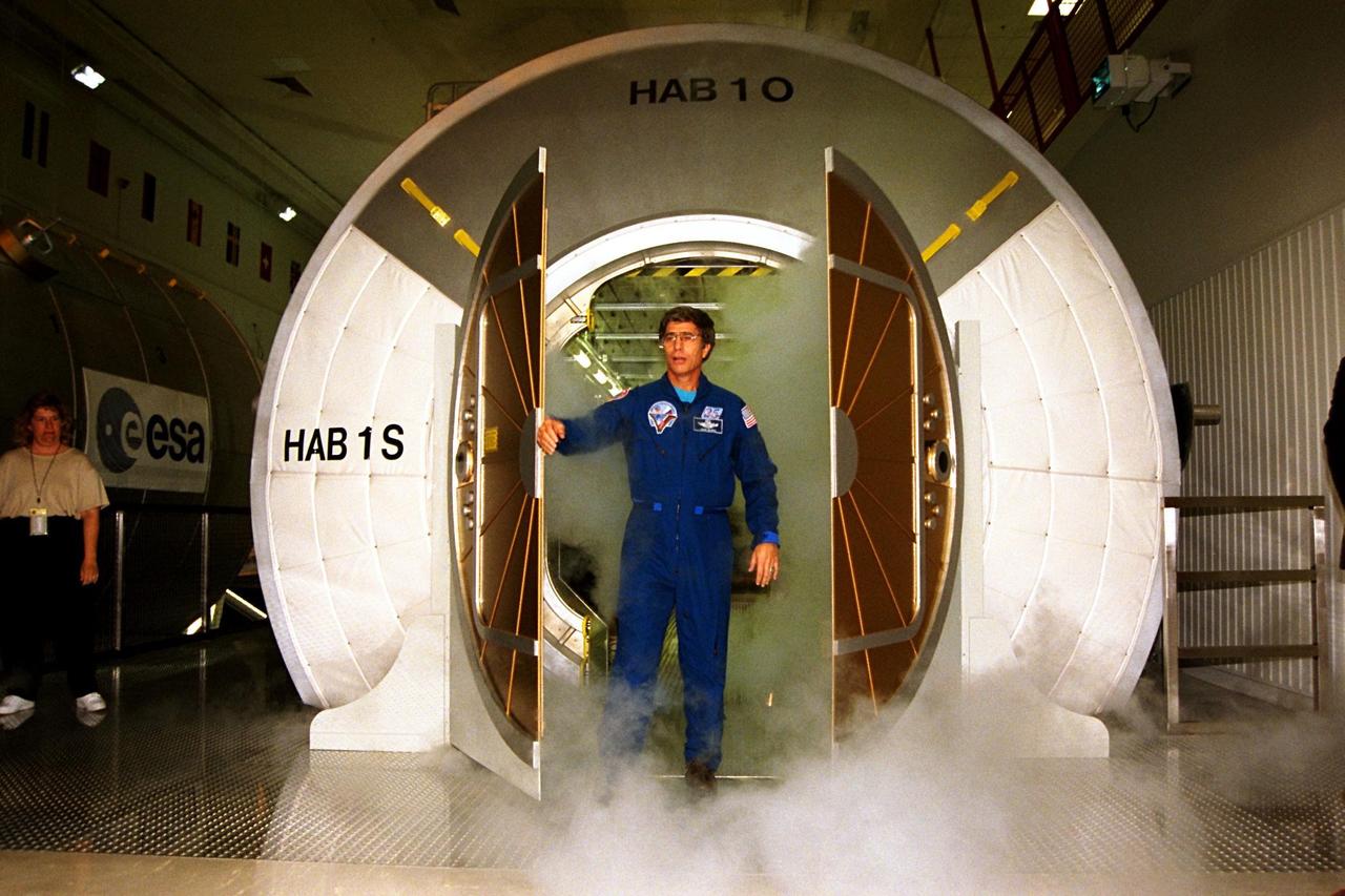 Retired Astronaut John Blaha celebrates the official opening of the new International Space Station (ISS) Center at Kennedy Space Center as he steps out of a full-scale mockup of one of the station modules. Modules through which visitors can walk that are included in the new tour attraction are the Habitation Unit, where station crew members will live, sleep, and work; a Laboratory Module; and the Pressurized Logistics Module, where racks and supplies will be transported back and forth from KSC to space. Guests also can take an elevated walkway to a gallery overlooking the work area where actual ISS hardware is prepared for flight into space. This new tour site, in addition to a new Launch Complex 39 Observation Gantry, are part of a comprehensive effort by NASA and Delaware North to expand and improve the KSC public tour and visitor facilities