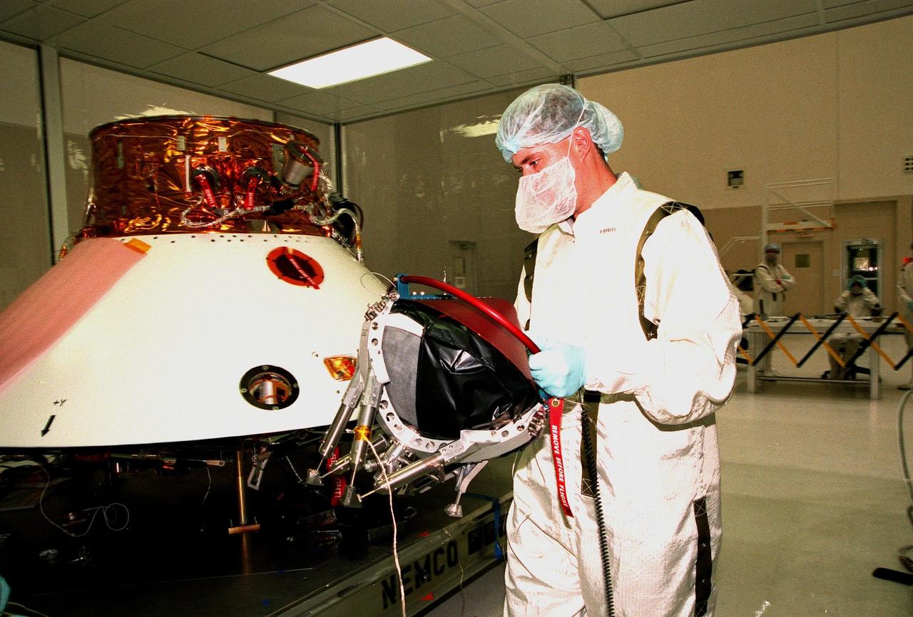 KENNEDY SPACE CENTER, FLA. -- In the Spacecraft Assembly and Encapsulation Facility -2 (SAEF-2), a JPL worker carries a Mars microprobe to the Mars Polar Lander at left. Two microprobes will hitchhike on the lander, scheduled to be launched Jan. 3, 1999, aboard a Delta II rocket. The solar-powered spacecraft is designed to touch down on the Martian surface near the northern-most boundary of the south pole in order to study the water cycle there. The lander also will help scientists learn more about climate change and current resources on Mars, studying such things as frost, dust, water vapor and condensates in the Martian atmosphere. The Mars microprobes, called Deep Space 2, are part of NASA's New Millennium Program. They will complement the climate-related scientific focus of the lander by demonstrating an advanced, rugged microlaser system for detecting subsurface water. Such data on polar subsurface water, in the form of ice, should help put limits on scientific projections for the global abundance of water on Mars