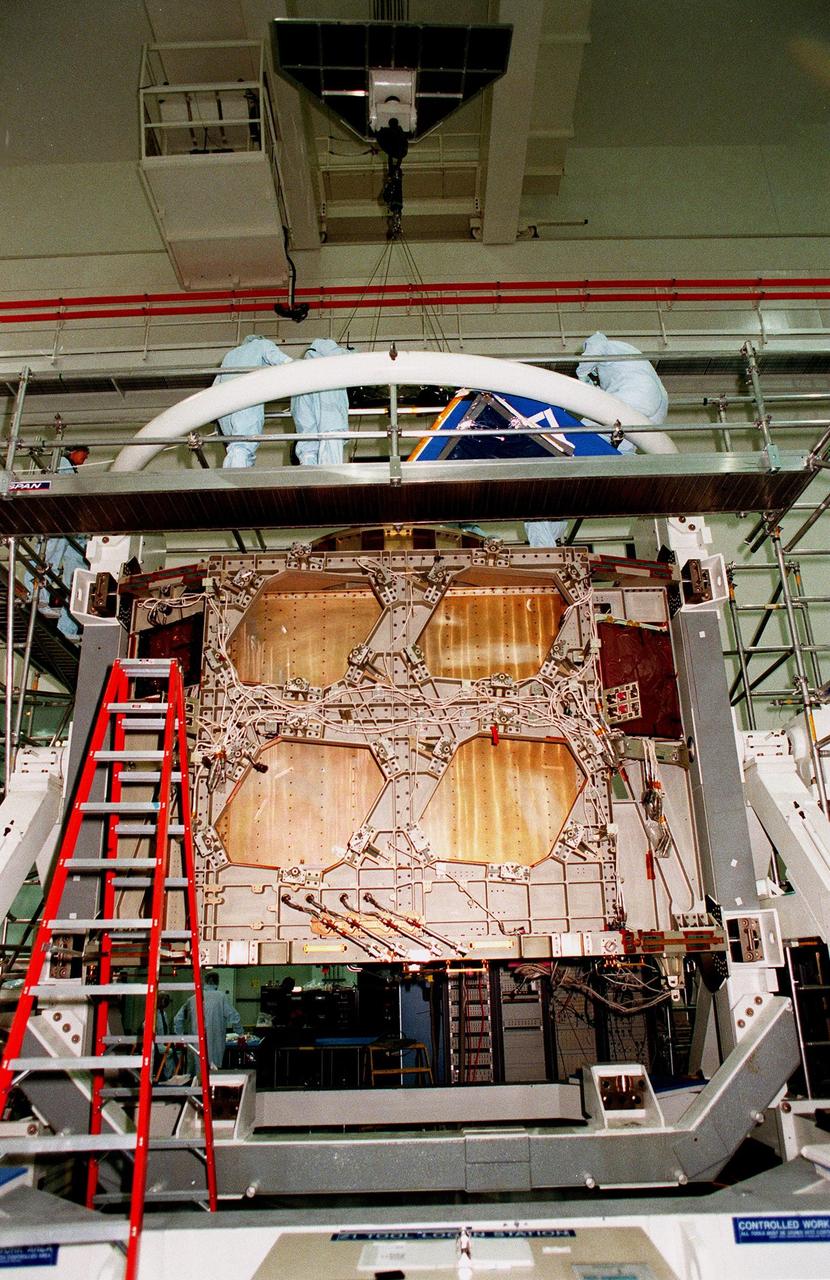Workers in the Space Station Processing Facility look at the Passive Common Berthing Mechanism (PCBM) that will be attached to the Z1 integrated truss structure, a component of the International Space Station (ISS). The truss will be used for the temporary installation of the P6 truss segment to the Unity connecting module. The P6 truss segment contains the solar arrays and batteries which will provide early station power. The truss is scheduled to be launched aboard STS-92 in late 1999