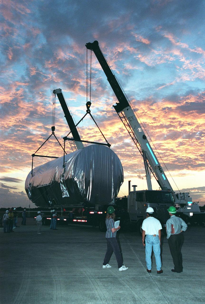 KENNEDY SPACE CENTER, FLA. -- In the growing dark of night, cranes maneuver the canister containing the U.S. laboratory module onto the bed of a trailer, waiting with its lights on for the move to the Space Station Processing Facility. Intended for the International Space Station, the lab is scheduled to undergo pre-launch preparations before its launch aboard the Shuttle Endeavour on mission STS-98. The laboratory comprises three cylindrical sections with two end cones. Each end-cone contains a hatch opening for entering and exiting the lab. The lab will provide a shirtsleeve environment for research in the areas of life science, microgravity science, Earth science and space science. Designated Flight 5A, this mission is targeted for launch in early 2000
