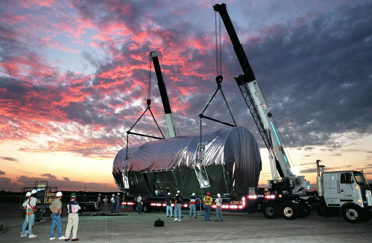 KENNEDY SPACE CENTER, FLA. -- In the last light before nightfall, workers watch as others check the fittings on the cranes lowering the container that encases U.S. laboratory module onto the bed of a trailer, waiting with its lights on for the move to the Space Station Processing Facility. Intended for the International Space Station, the lab is scheduled to undergo pre-launch preparations before its launch aboard the Shuttle Endeavour on mission STS-98. The laboratory comprises three cylindrical sections with two end cones. Each end-cone contains a hatch opening for entering and exiting the lab. The lab will provide a shirtsleeve environment for research in the areas of life science, microgravity science, Earth science and space science. Designated Flight 5A, this mission is targeted for launch in early 2000