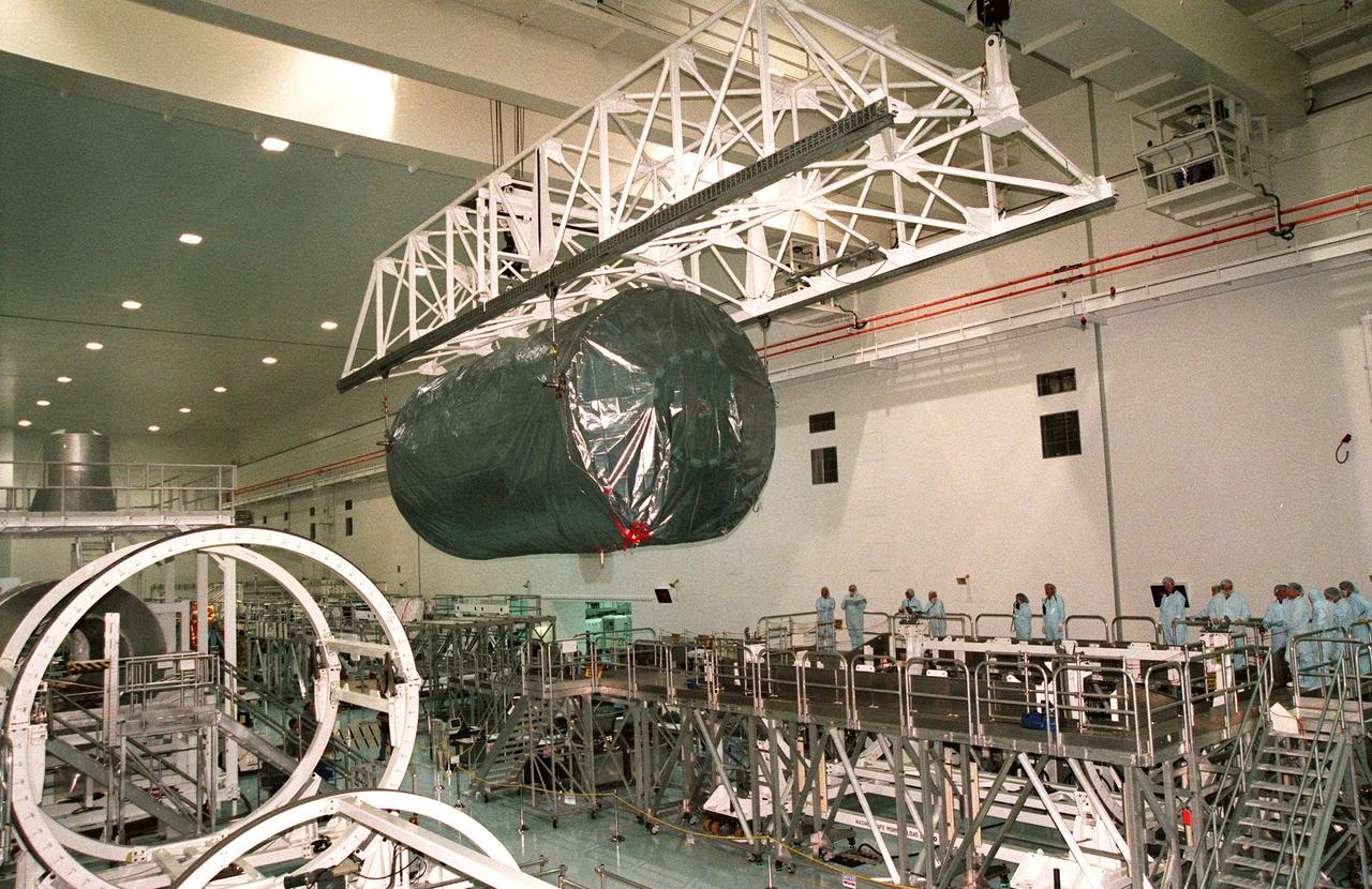 KENNEDY SPACE CENTER, FLA. -- An overhead crane in the high bay of the Space Station Processing Facility moves the U.S. laboratory module, an element of the International Space Station, toward the workstand on the right. KSC workers watch its movement. The lab will undergo pre-launch preparations before its launch aboard the Shuttle Endeavour on mission STS-98. The laboratory comprises three cylindrical sections with two end cones. Each end-cone contains a hatch opening for entering and exiting the lab. The lab will provide a shirtsleeve environment for research in the areas of life science, microgravity science, Earth science and space science. Designated Flight 5A, this mission is targeted for launch in early 2000