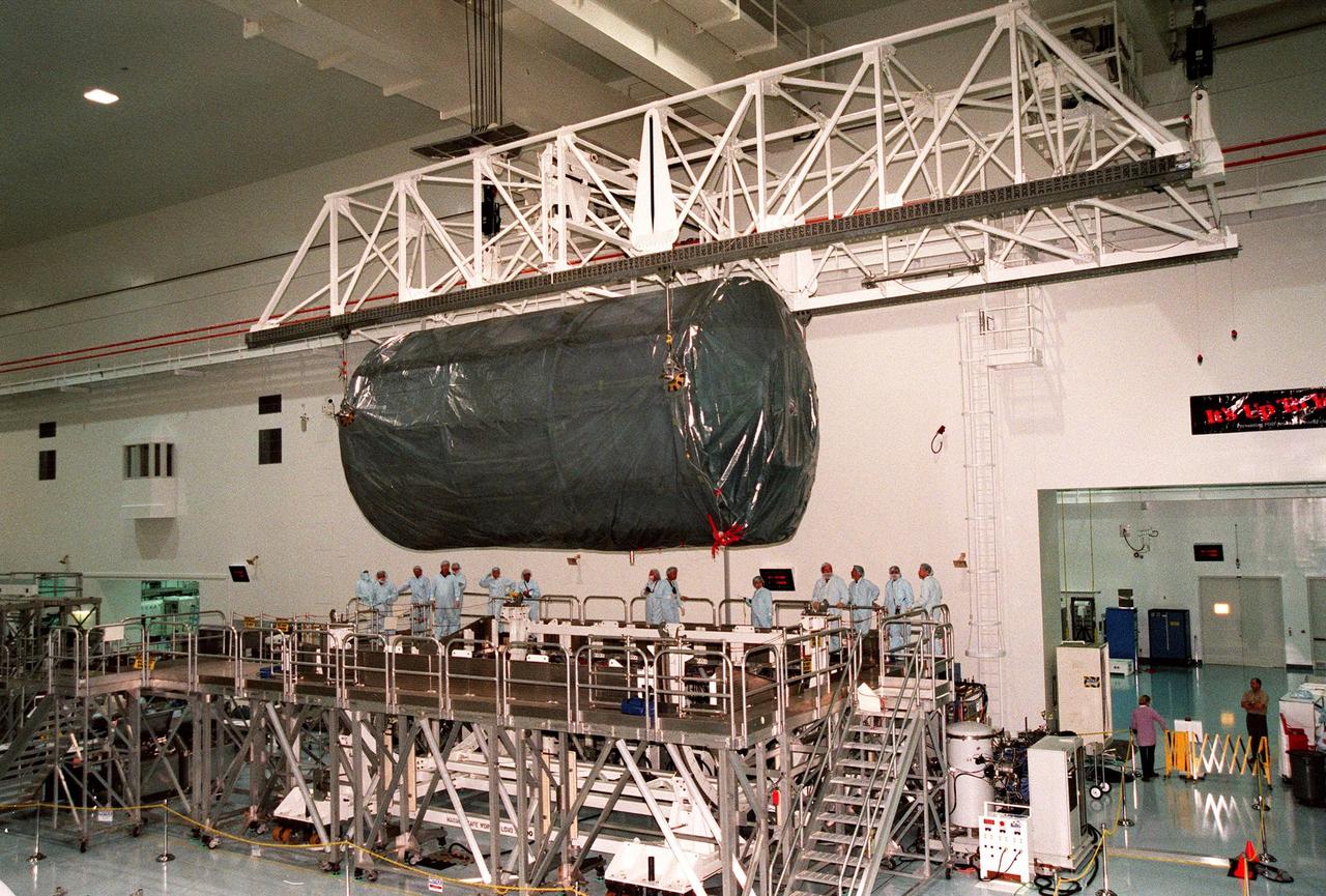 KENNEDY SPACE CENTER, FLA. -- An overhead crane in the high bay of the Space Station Processing Facility lowers the U.S. laboratory module, an element of the International Space Station, onto the workstand as KSC workers watch. The lab will undergo pre-launch preparations before its launch aboard the Shuttle Endeavour on mission STS-98. The laboratory comprises three cylindrical sections with two end cones. Each end-cone contains a hatch opening for entering and exiting the lab. The lab will provide a shirtsleeve environment for research in the areas of life science, microgravity science, Earth science and space science. Designated Flight 5A, this mission is targeted for launch in early 2000