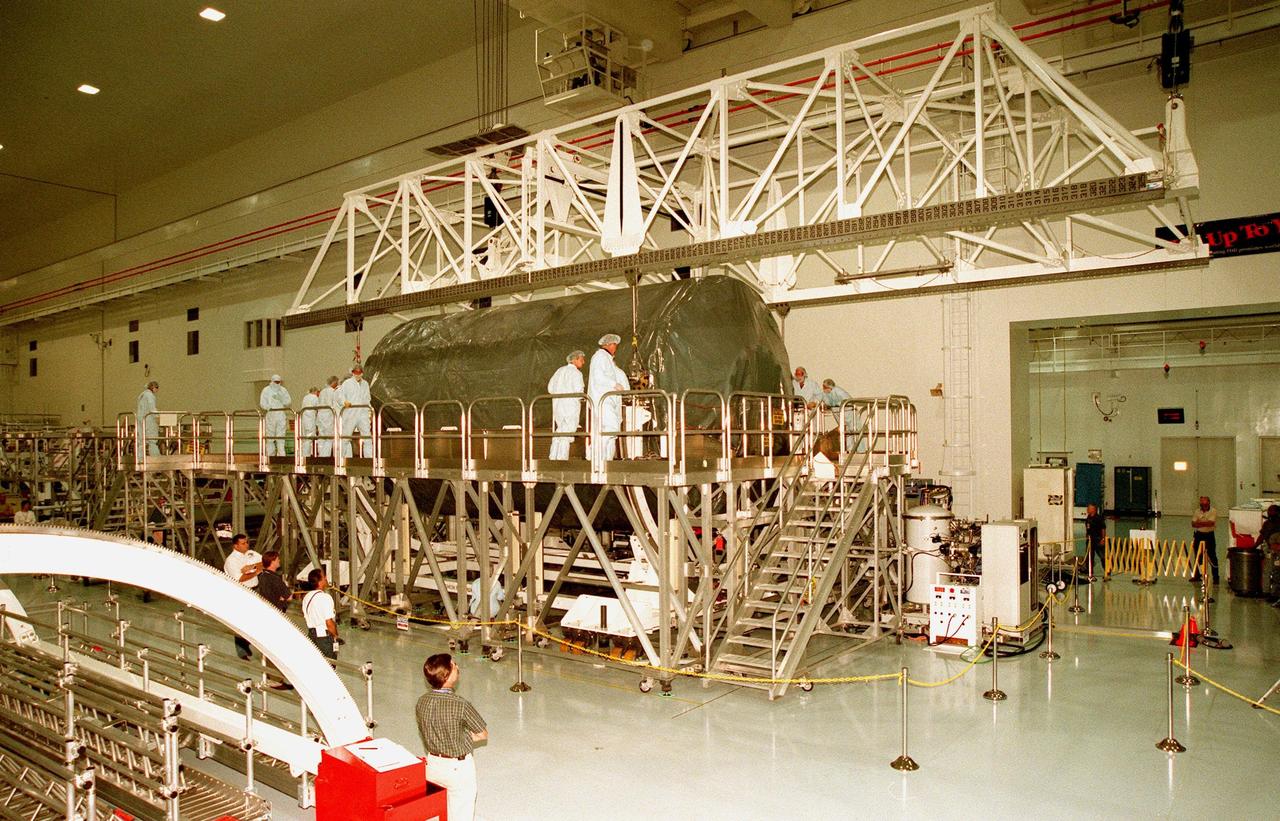 KENNEDY SPACE CENTER, FLA. -- KSC workers watch as an overhead crane in the high bay of the Space Station Processing Facility lowers the U.S. laboratory module, an element of the International Space Station, onto the workstand. The lab will undergo pre-launch preparations before its launch aboard the Shuttle Endeavour on mission STS-98. The laboratory comprises three cylindrical sections with two end cones. Each end-cone contains a hatch opening for entering and exiting the lab. The lab will provide a shirtsleeve environment for research in the areas of life science, microgravity science, Earth science and space science. Designated Flight 5A, this mission is targeted for launch in early 2000
