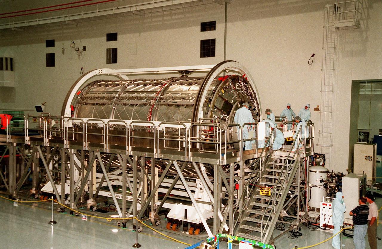 KENNEDY SPACE CENTER, FLA. -- On a workstand in the Space Station Processing Facility, KSC workers take a look at the U.S. laboratory module, an element of the International Space Station, after its protective cover has been removed. The lab will undergo pre-launch preparations before its launch aboard the Shuttle Endeavour on mission STS-98. The laboratory comprises three cylindrical sections with two end cones. Each end-cone contains a hatch opening for entering and exiting the lab. The lab will provide a shirtsleeve environment for research in the areas of life science, microgravity science, Earth science and space science. Designated Flight 5A, this mission is targeted for launch in early 2000