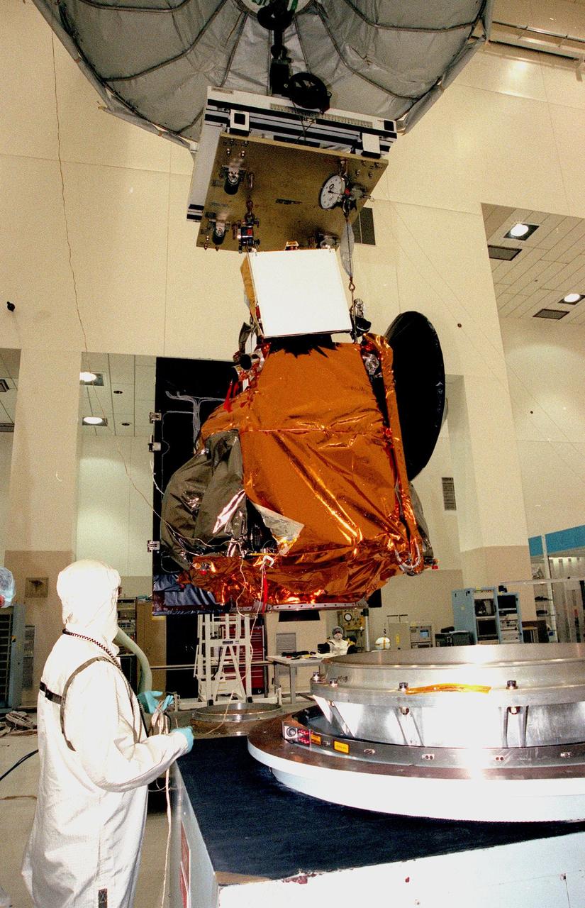 KENNEDY SPACE CENTER, FLA. -- In the Spacecraft Assembly and Encapsulation Facility -2 (SAEF-2), a worker maneuvers the Mars Climate Orbiter, suspended by an overhead crane, to the spin test equipment at lower right. Targeted for launch aboard a Delta II rocket on Dec. 10, 1998, the orbiter is heading for Mars where it will primarily support its companion Mars Polar Lander spacecraft, which is planned for launch on Jan. 3, 1999. The orbiter's instruments will monitor the Martian atmosphere and image the planet's surface on a daily basis for 687 Earth days. It will observe the appearance and movement of atmospheric dust and water vapor, as well as characterize seasonal changes on the surface. The detailed images of the surface features will provide important clues to the planet's early climate history and give scientists more information about possible liquid water reserves beneath the surface