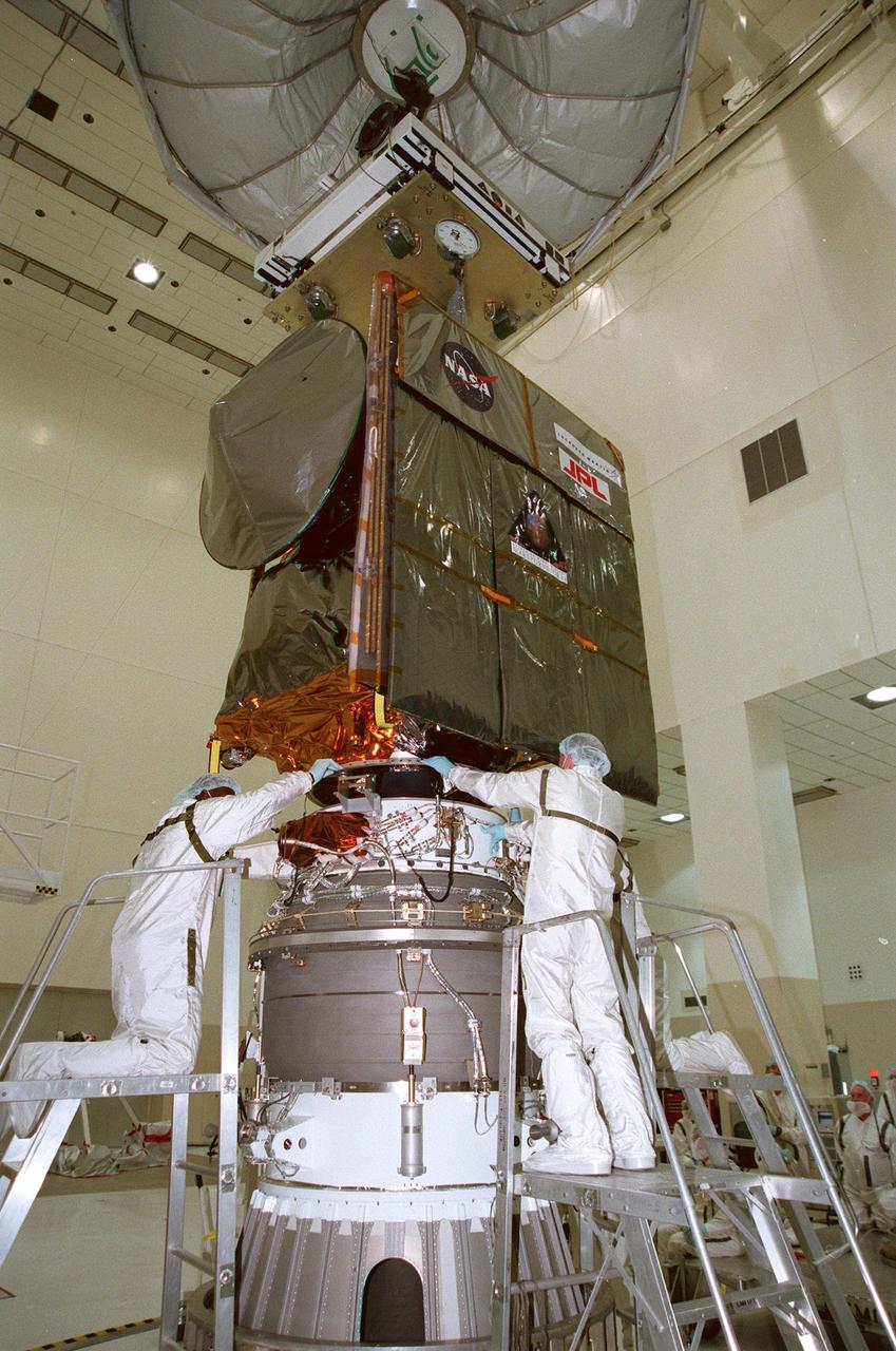 KENNEDY SPACE CENTER, FLA. -- In the Spacecraft Assembly and Encapsulation Facility -2 (SAEF-2), workers check on the fitting between the Mars Climate Orbiter (above) and the third stage of the Boeing Delta II launch vehicle (below). The third stage is a solid-propellant Thiokol Star 48B booster, the same final stage used in the 1996 launch of Mars Global Surveyor. Targeted for launch on Dec. 10, 1998, the orbiter is heading for Mars where it will primarily support its companion Mars Polar Lander spacecraft, which is planned for launch on Jan. 3, 1999. The orbiter's instruments will monitor the Martian atmosphere and image the planet's surface on a daily basis for 687 Earth days. It will observe the appearance and movement of atmospheric dust and water vapor, as well as characterize seasonal changes on the surface. The detailed images of the surface features will provide important clues to the planet's early climate history and give scientists more information about possible liquid water reserves beneath the surface