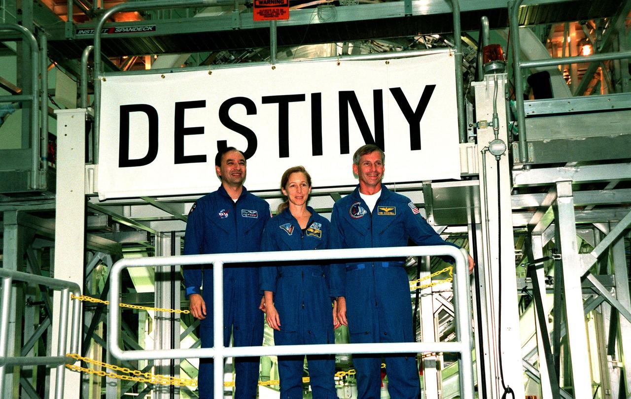 KENNEDY SPACE CENTER, FLA. -- In the Space Station Processing Facility, STS-98 crew members Pilot Mark Polansky, Mission Specialist Marsha Ivins and Commander Ken Cockrell pose underneath the banner revealing the name Destiny given to the U.S. Lab module. They are part of the five-member crew scheduled to carry the lab into space aboard Space Shuttle Endeavour early in the year 2000 where it will become the centerpiece of scientific research on the International Space Station. The Shuttle will spend six days docked to the station while the laboratory is attached and three space walks are conducted to complete its assembly. The laboratory will be launched with five equipment racks aboard, which will provide essential functions for station systems, including high data-rate communications, and maintain the station's orientation using control gyroscopes launched earlier. Additional equipment and research racks will be installed in the laboratory on subsequent Shuttle flights