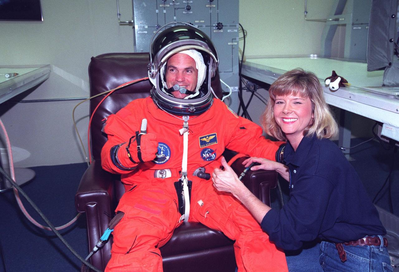 In the Operations and Checkout Building, STS-88 Pilot Frederick W. "Rick" Sturckow gets help with his flight suit from suit technician Terri McKinney before launch. Mission STS-88 is expected to launch at 3:56 a.m. EST with the six-member crew aboard Space Shuttle Endeavour on Dec. 3. Endeavour carries the Unity connecting module, which the crew will be mating with the Russian-built Zarya control module already in orbit. In addition to Unity, two small replacement electronics boxes are on board for possible repairs to Zarya batteries. The mission is expected to last 11 days, 19 hours and 49 minutes, landing at 10:17 p.m. EST on Dec. 14