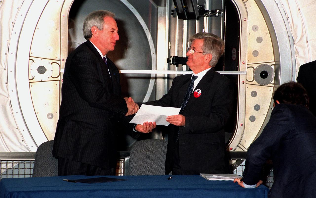 KENNEDY SPACE CENTER, FLA.  --  Sergio De Julio (at right), president of the Italian Space Agency, Agenzia Spaziale Italiana (ASI), shakes the hand of NASA Adminstrator Daniel S. Goldin while holding the document which signifies the transfer of the "Leonardo" Multipurpose Logistics Module (MPLM) from ASI to NASA. The ceremonial event was held in the Space Station Processing Facility beside Leonardo. The MPLM, a reusable logistics carrier, will be the primary delivery system used to resupply and return International Space Station cargo requiring a pressurized environment. Leonardo is the first of three MPLM carriers for the International Space Station. It is scheduled to be launched on Space Shuttle Mission STS-100, targeted for April 2000