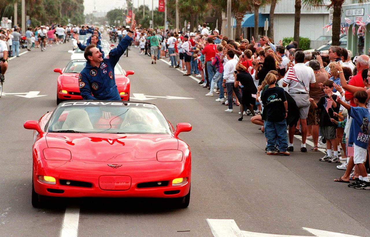 STS-95 Commander Curtis L. Brown Jr. (in front), along with the other crew members behind him, waves to the crowd as he leads a parade of 1999 C-5 Corvette convertibles down State Road A1A in nearby Cocoa Beach. Organizers of the parade include the Cocoa Beach Area Chamber of Commerce, the Brevard County Tourist Development Council, and the cities of Cape Canaveral and Cocoa Beach. The parade is reminiscent of those held after missions during the Mercury Program