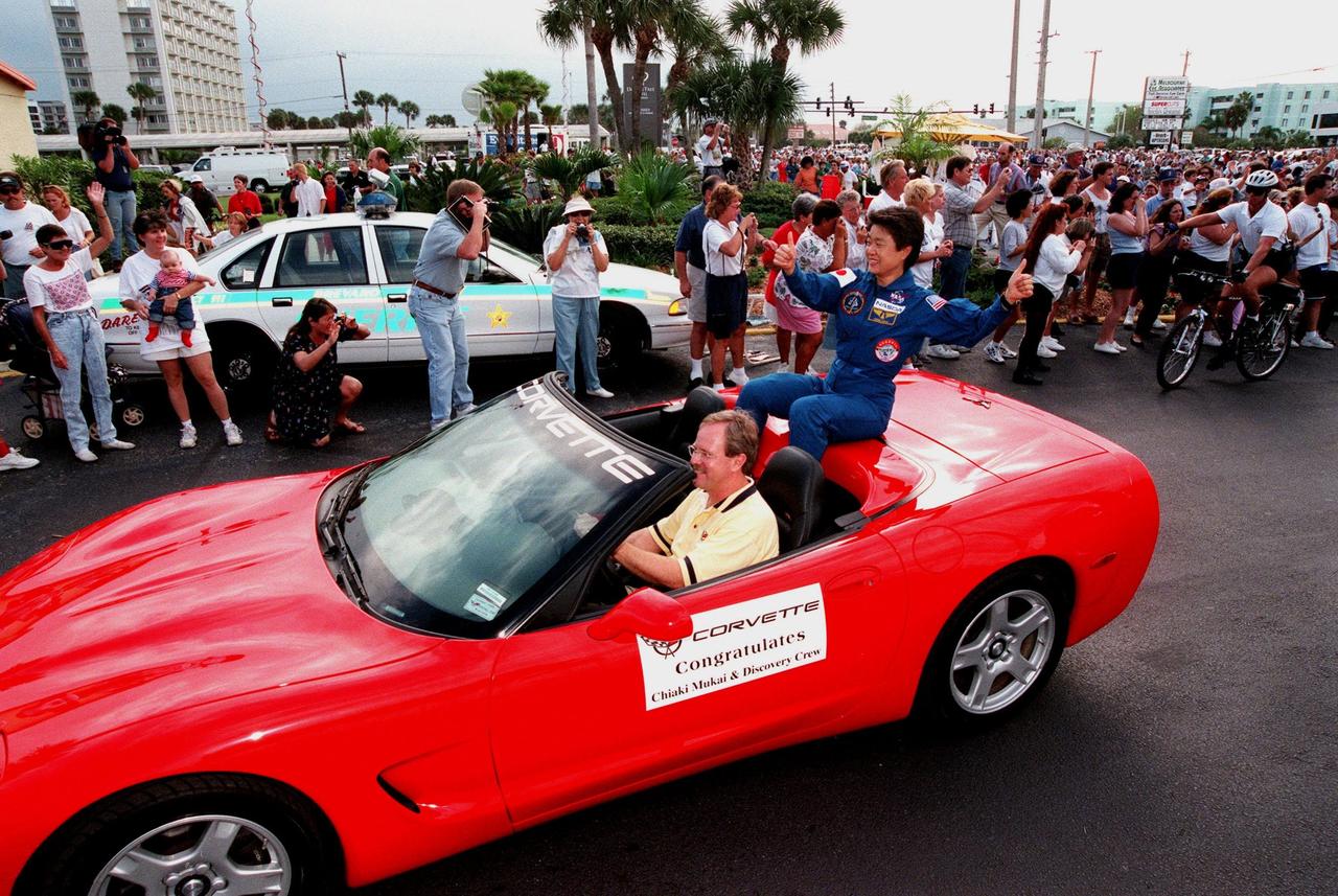 STS-95 Payload Specialist Chiaki Mukai is perched on the back of a red 1999 C-5 Corvette convertible during a parade down State Road A1A in nearby Cocoa Beach. Organizers of the parade include the Cocoa Beach Area Chamber of Commerce, the Brevard County Tourist Development Council, and the cities of Cape Canaveral and Cocoa Beach. The parade is reminiscent of those held after missions during the Mercury Program