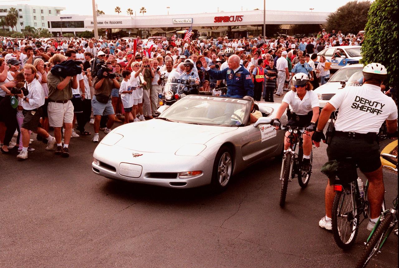 STS-95 Payload Specialist John H. Glenn Jr. waves to a dense crowd of well-wishers from the back of a silver 1999 C-5 Corvette convertible during a parade down State Road A1A in nearby Cocoa Beach. Organizers of the parade include the Cocoa Beach Area Chamber of Commerce, the Brevard County Tourist Development Council, and the cities of Cape Canaveral and Cocoa Beach. The parade is reminiscent of those held after missions during the Mercury Program
