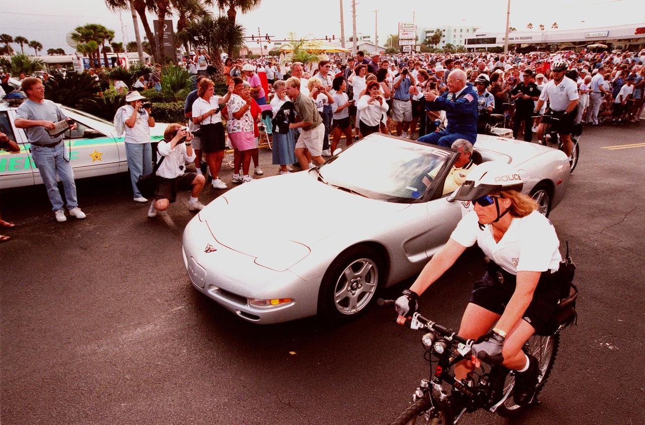 STS-95 Payload Specialist John H. Glenn Jr. waves to spectators from the back of a silver 1999 C-5 Corvette convertible during a parade down State Road A1A in nearby Cocoa Beach. Organizers of the parade include the Cocoa Beach Area Chamber of Commerce, the Brevard County Tourist Development Council, and the cities of Cape Canaveral and Cocoa Beach. The parade is reminiscent of those held after missions during the Mercury Program